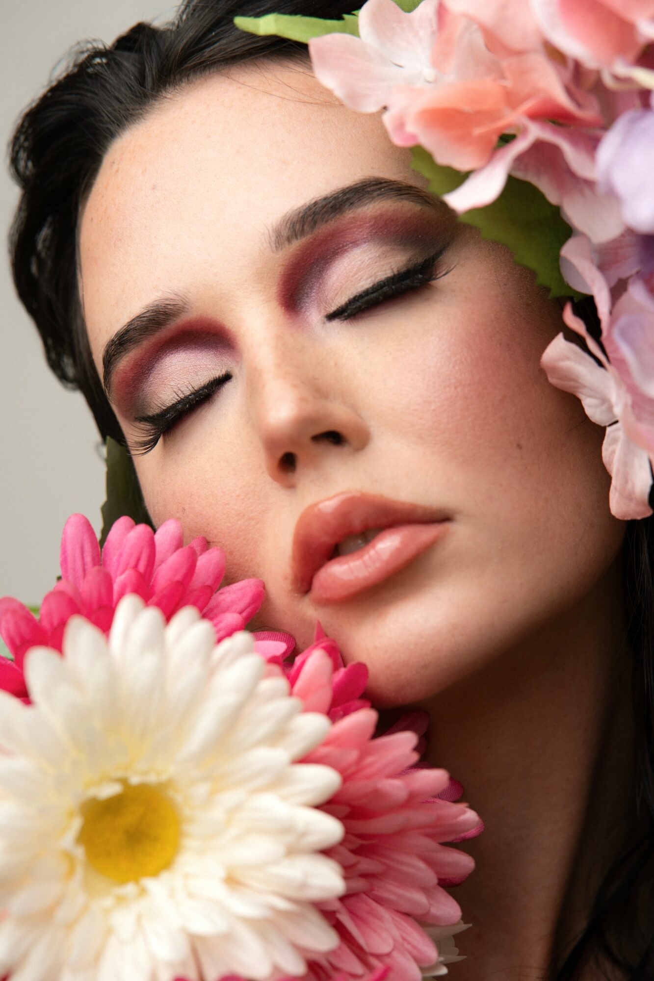 Close-up of a woman with closed eyes surrounded by pink and white flowers.