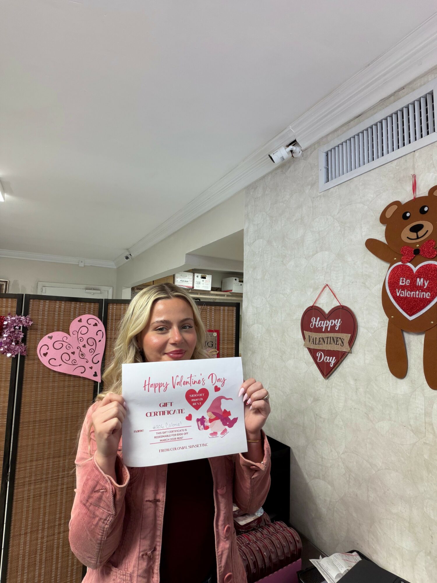 Woman holding a Valentine's Day certificate in a room decorated with heart and bear Valentine's decorations.