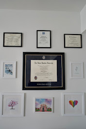 Wall with framed certificates and colorful artwork, including a large central diploma, arranged in a grid pattern.