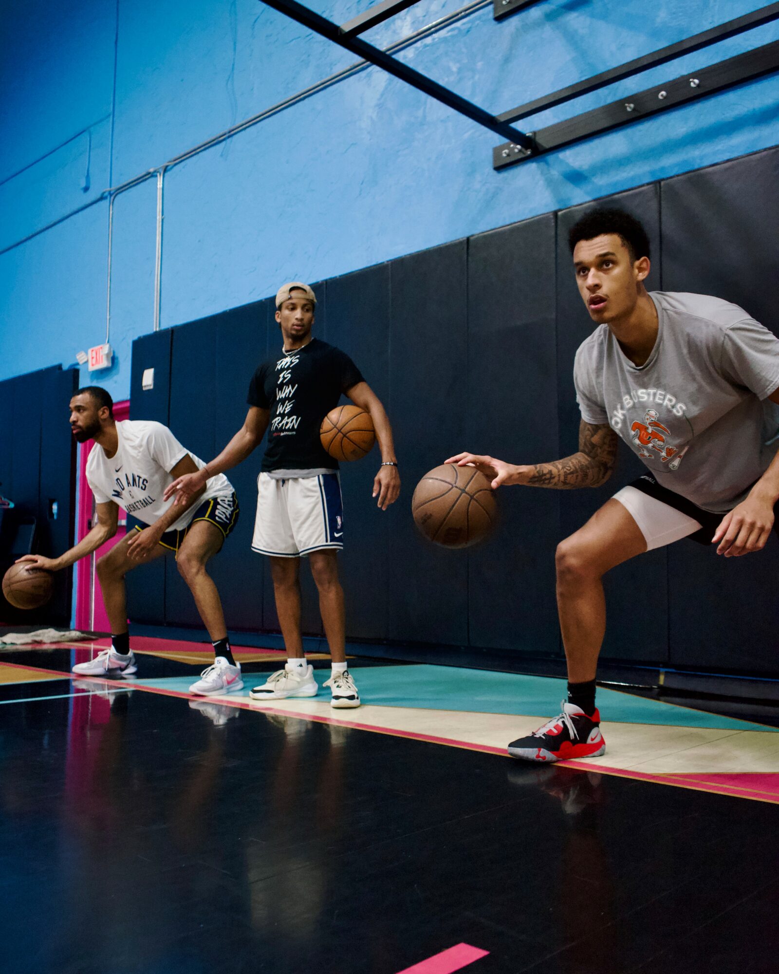 Three people practicing basketball drills in a gym, holding basketballs and wearing athletic clothing.