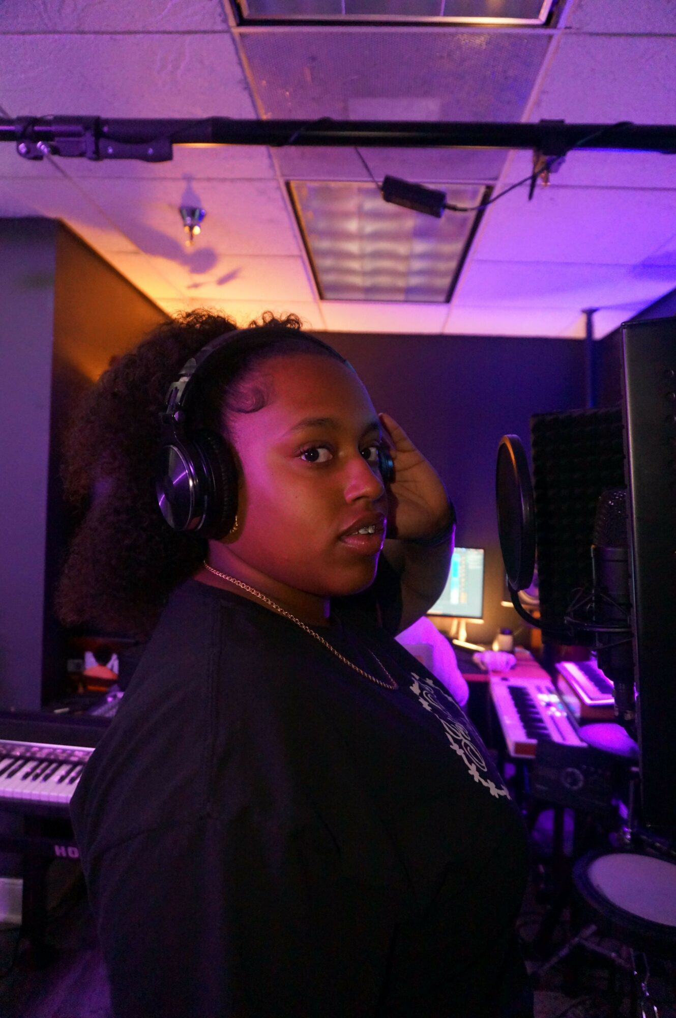 Person wearing headphones lying in a dimly lit room with purple lighting, looking at the camera.