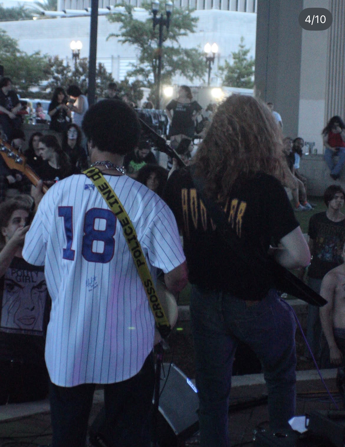 Two people standing with their backs to the camera in a crowded indoor space, one wearing a striped shirt with the number 18, the other in a black shirt.