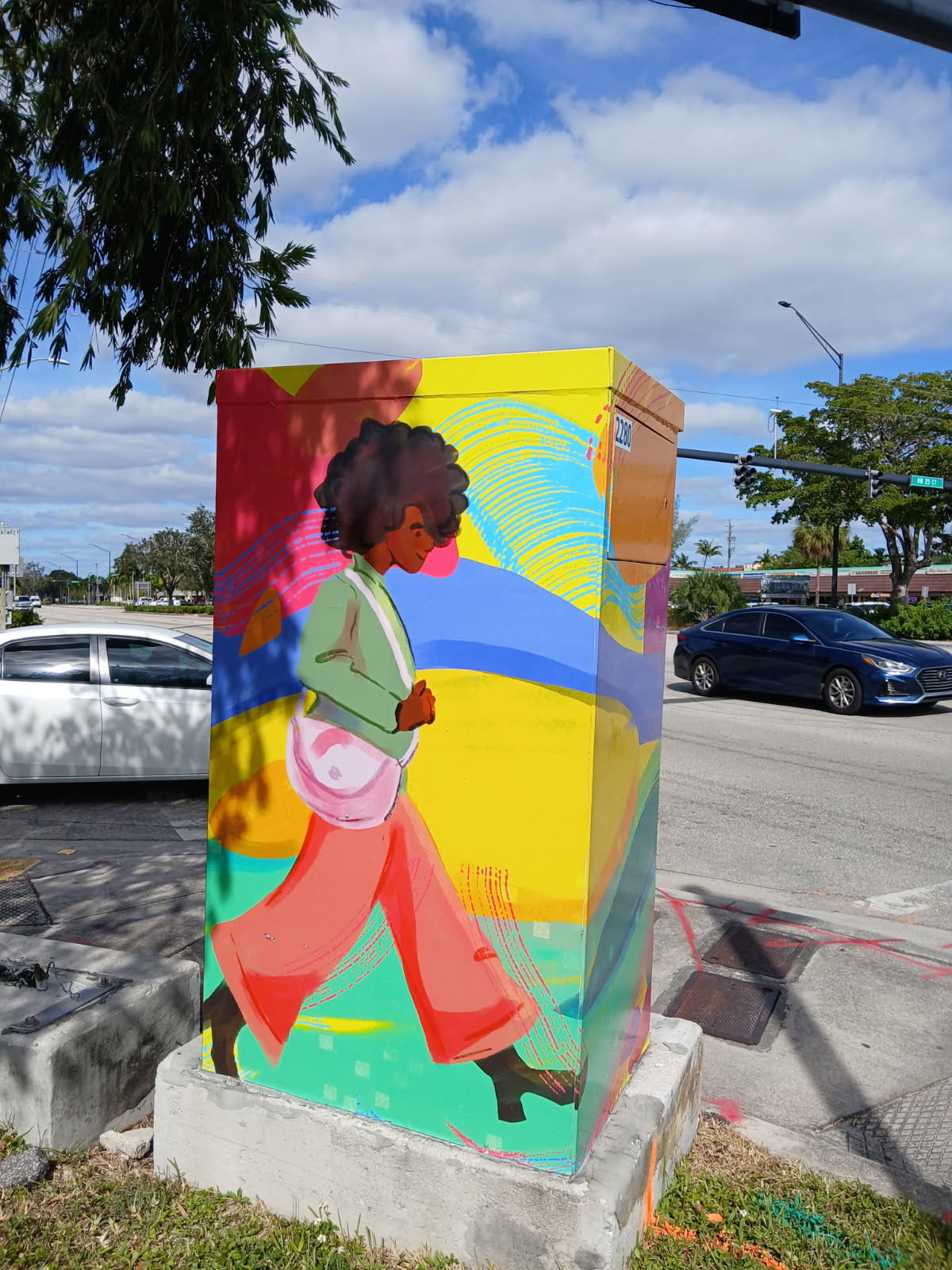 Colorful mural of a woman walking with a bag, painted on a utility box outdoors, with trees and cars in background.