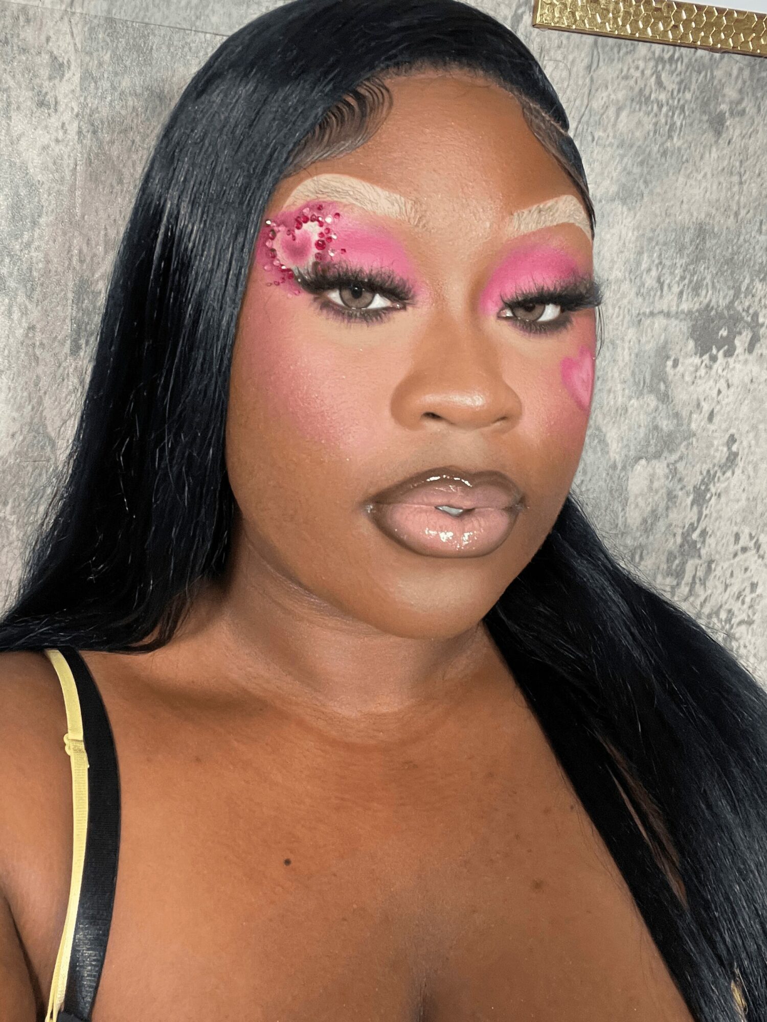 Close-up of a woman with long black hair, pink eye makeup with floral designs, and glossy lips.