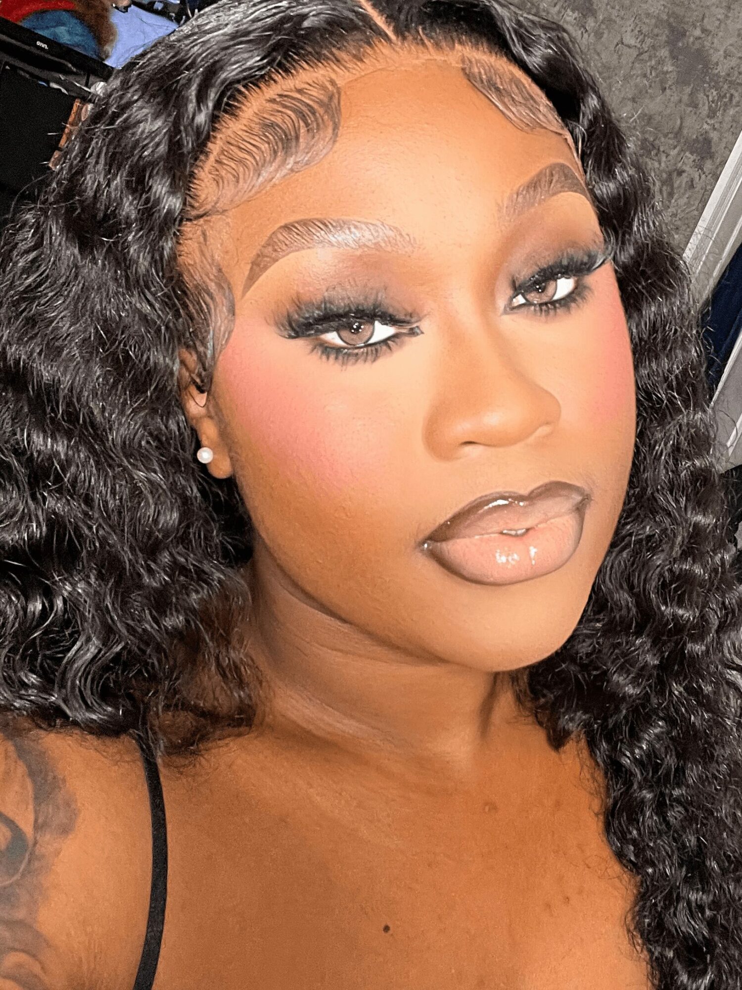 Close-up of a woman with styled curly hair, makeup, and earrings, looking at the camera.