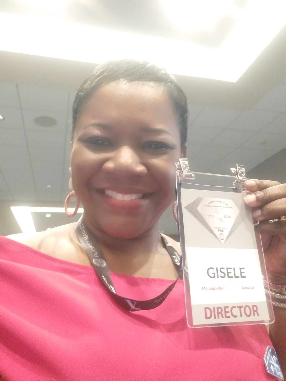 Woman smiling holding a name badge that reads GISELE, with a 'DIRECTOR' label, in an indoor setting.