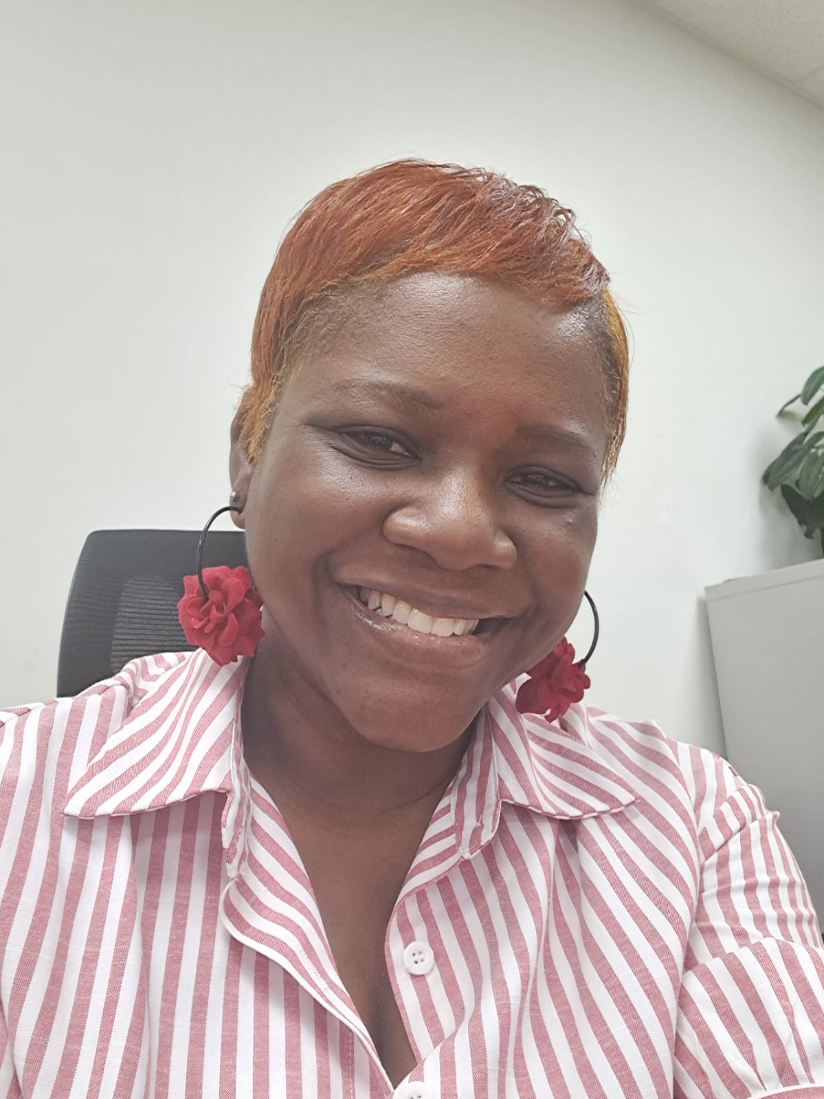 Smiling woman with short, reddish hair wearing a striped shirt and red earrings, sitting in an office.