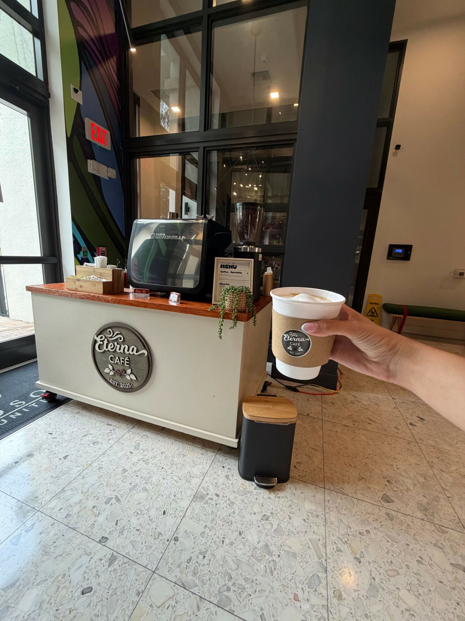 Person holding a Starbucks coffee cup near a counter inside a cafe, with a window and interior visible.