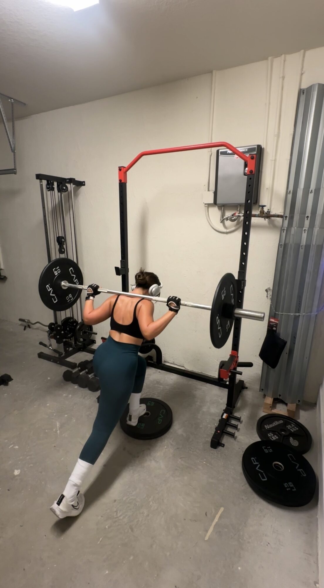 Person performing a squat exercise with a barbell in a home gym, facing away from the camera.