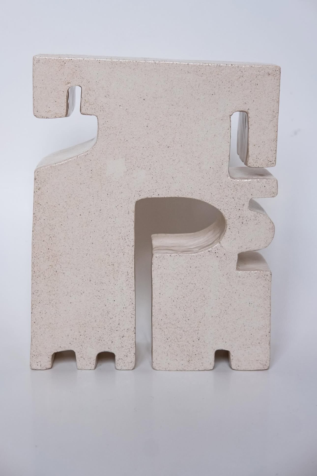 Concrete sculpture with geometric cutouts and protrusions, standing upright against a plain background.