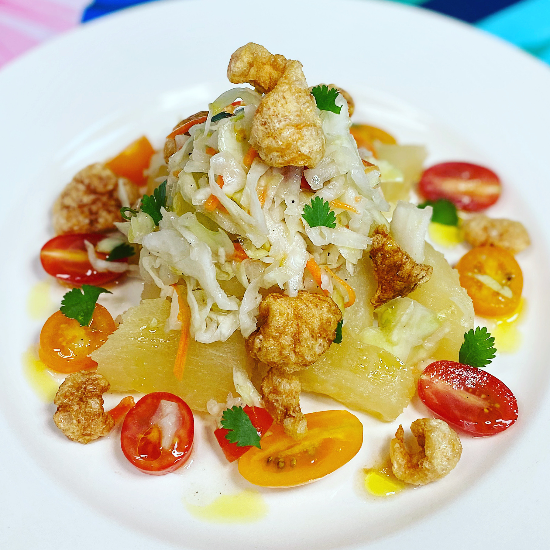 Salad with shredded vegetables, cherry tomatoes, pineapple chunks, fried chicken pieces, and cilantro on a white plate.