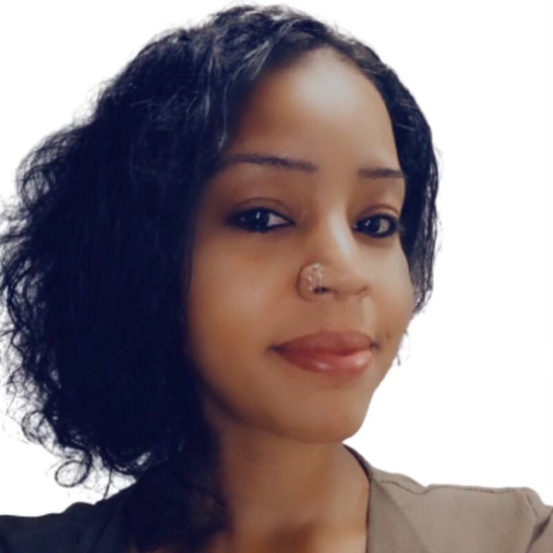 Young woman with curly black hair, nose piercing, and a slight smile, against a white background.