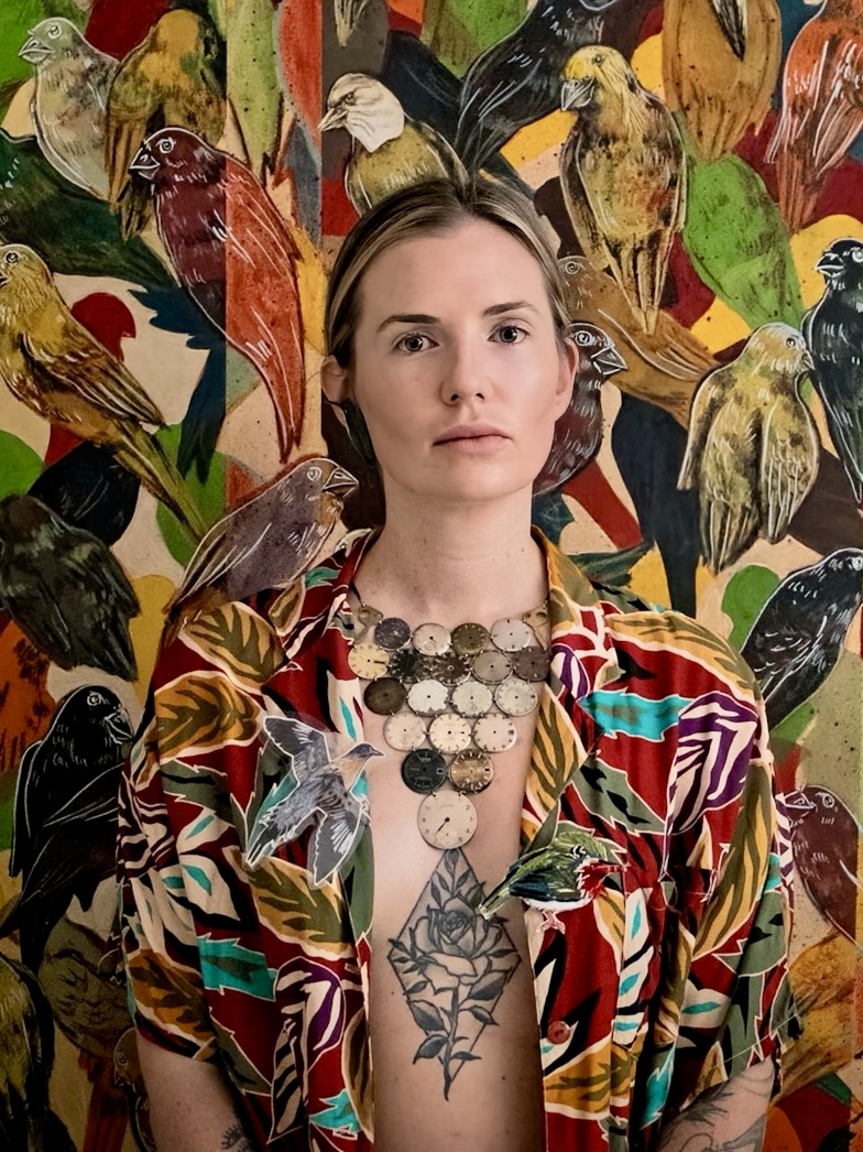 Woman with short hair and a colorful patterned shirt, surrounded by various colorful birds in the background.