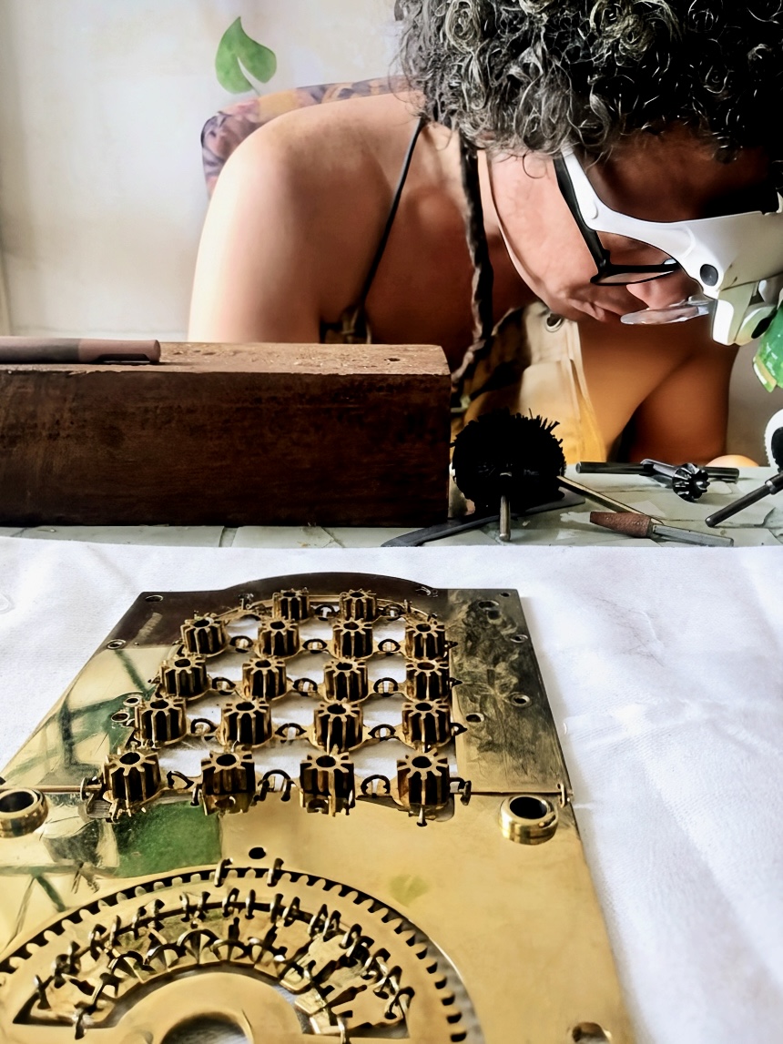 Person with curly hair and glasses examining a circuit board with a magnifying tool, leaning over a table.