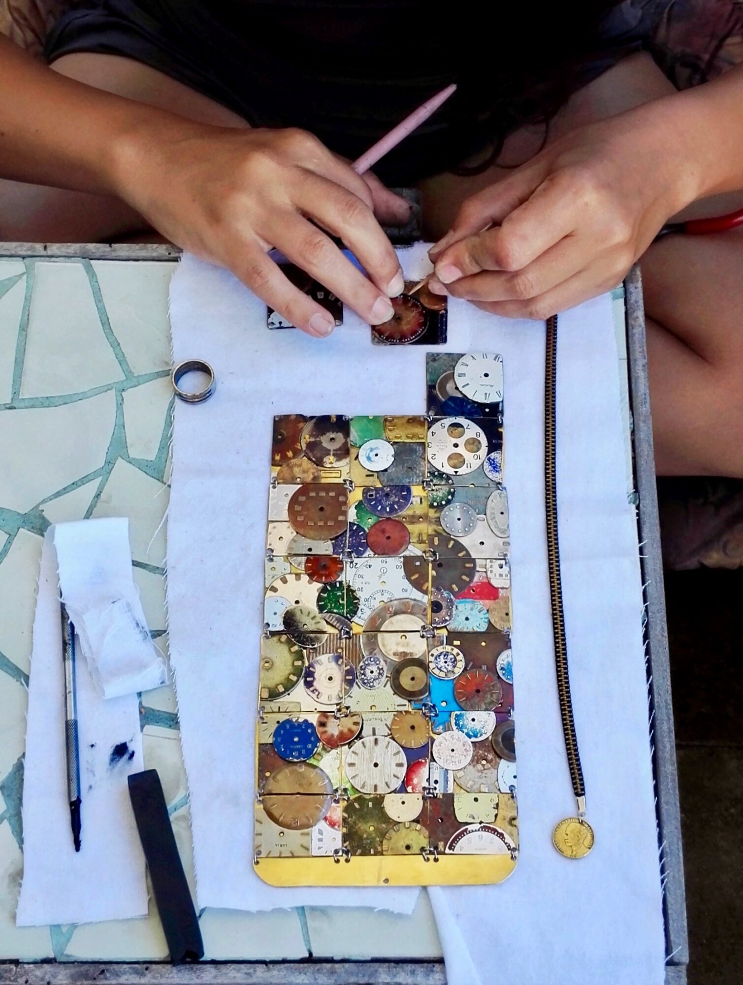 Person's hands working on a sewing project with buttons on a fabric piece, on a table with sewing tools.