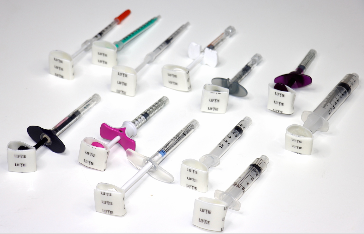 Multiple syringes with different colored needles and caps, arranged on a white surface, with labels attached to the syringe barrels.