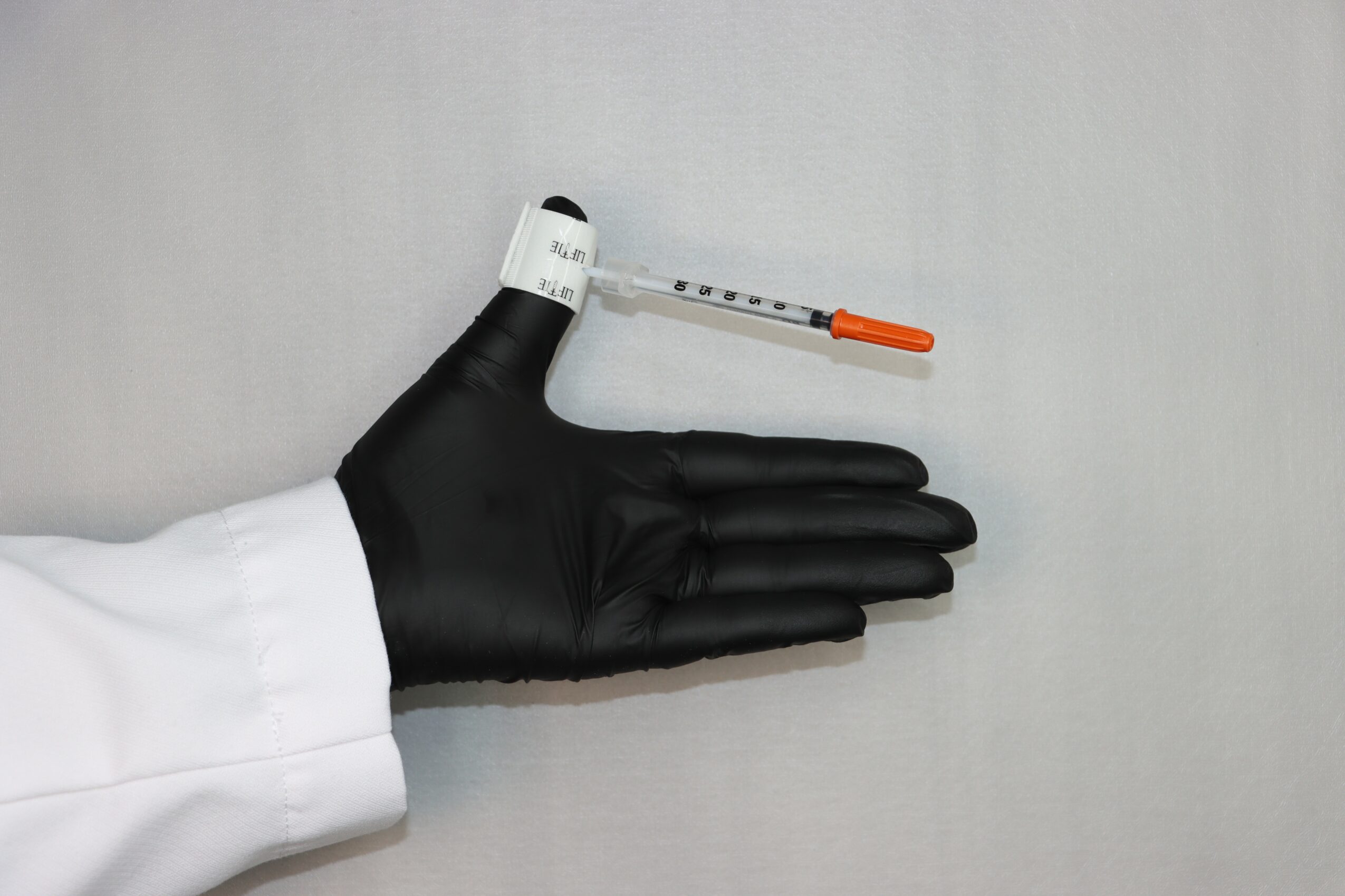 A gloved hand holding a syringe with an orange cap, against a plain background.