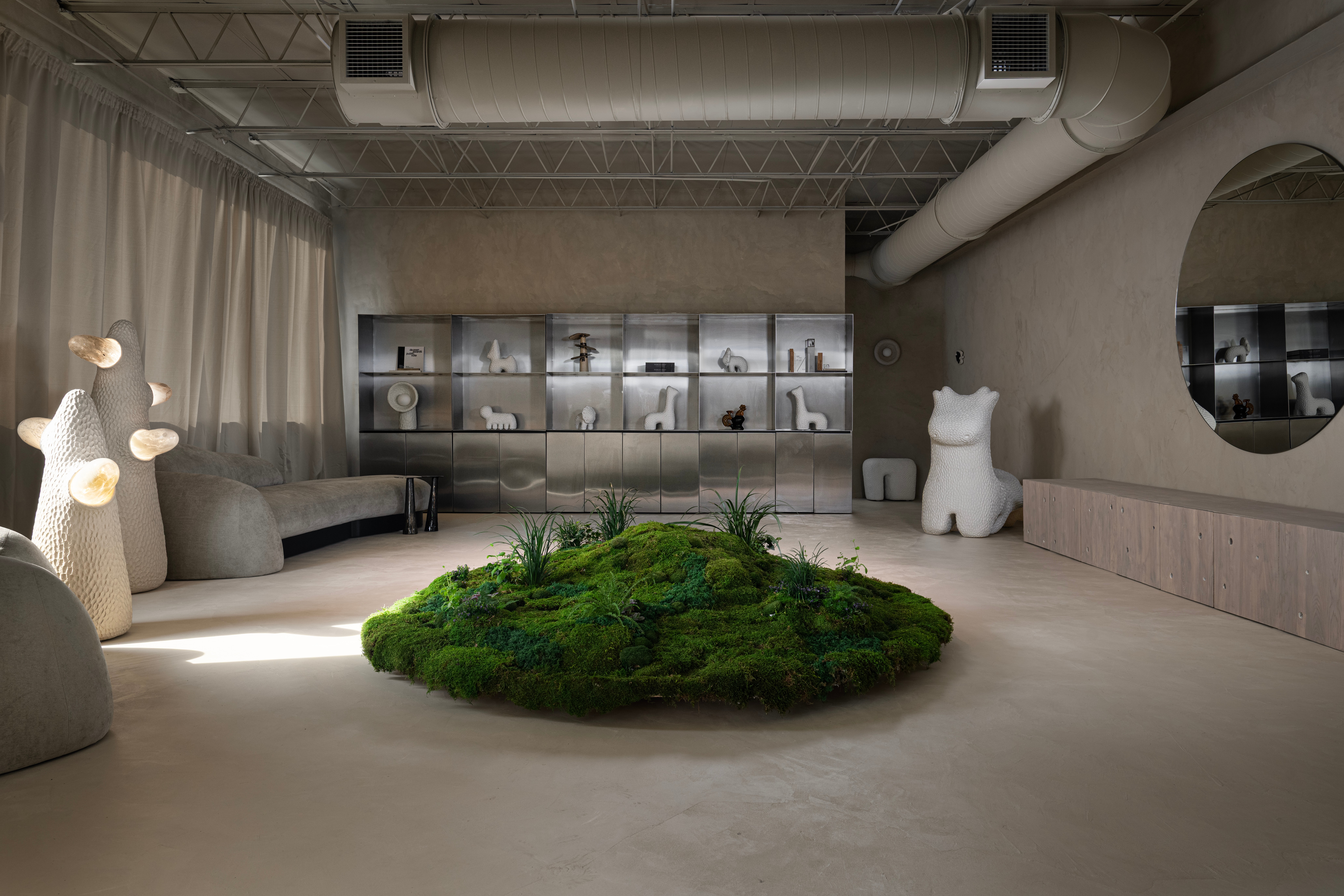 Modern interior with a moss centerpiece, seating area, shelves, and decorative objects, in neutral tones with natural light.