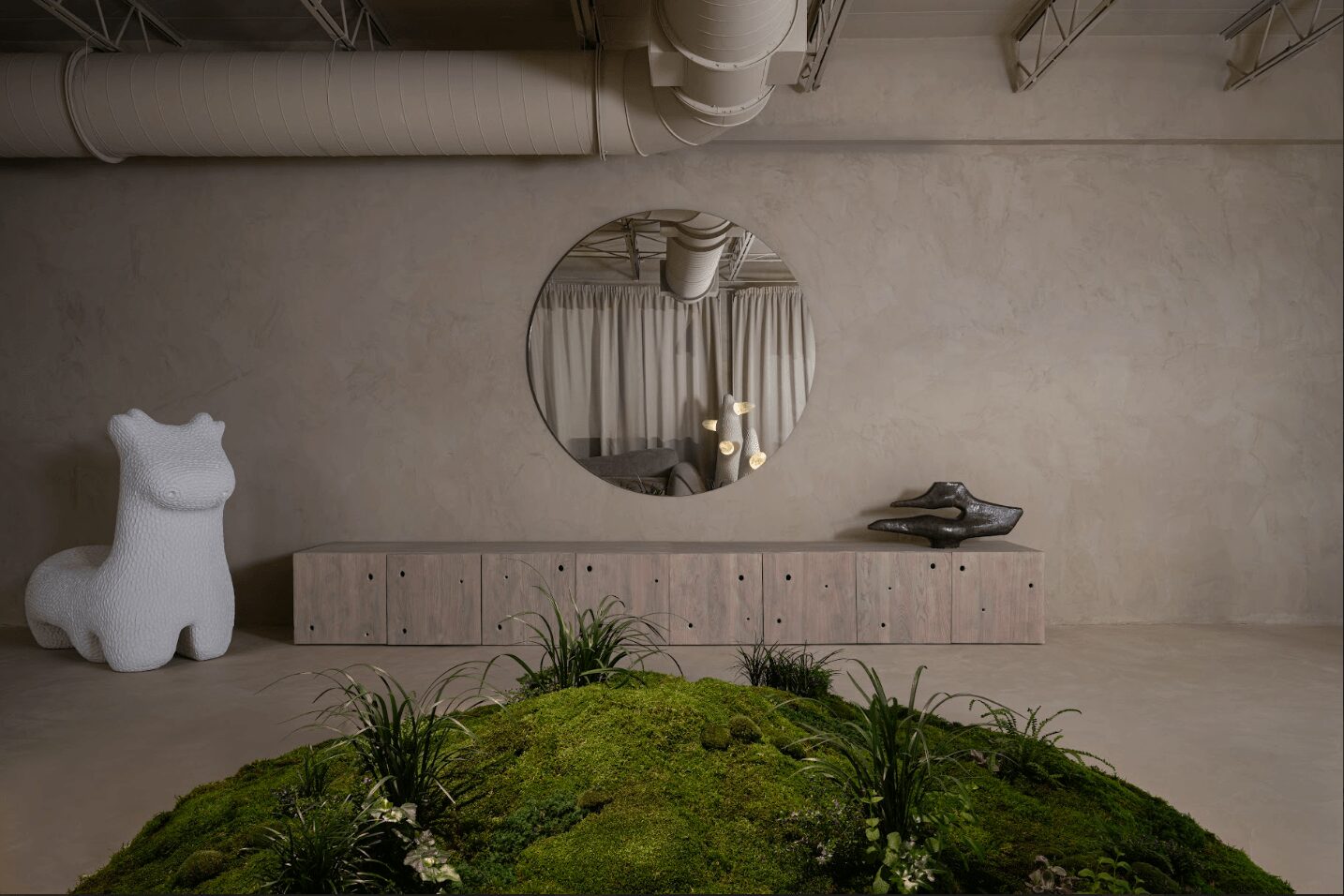 Interior space with a round mirror, a dog-shaped sculpture, a long cabinet, and plants on a moss-covered surface.