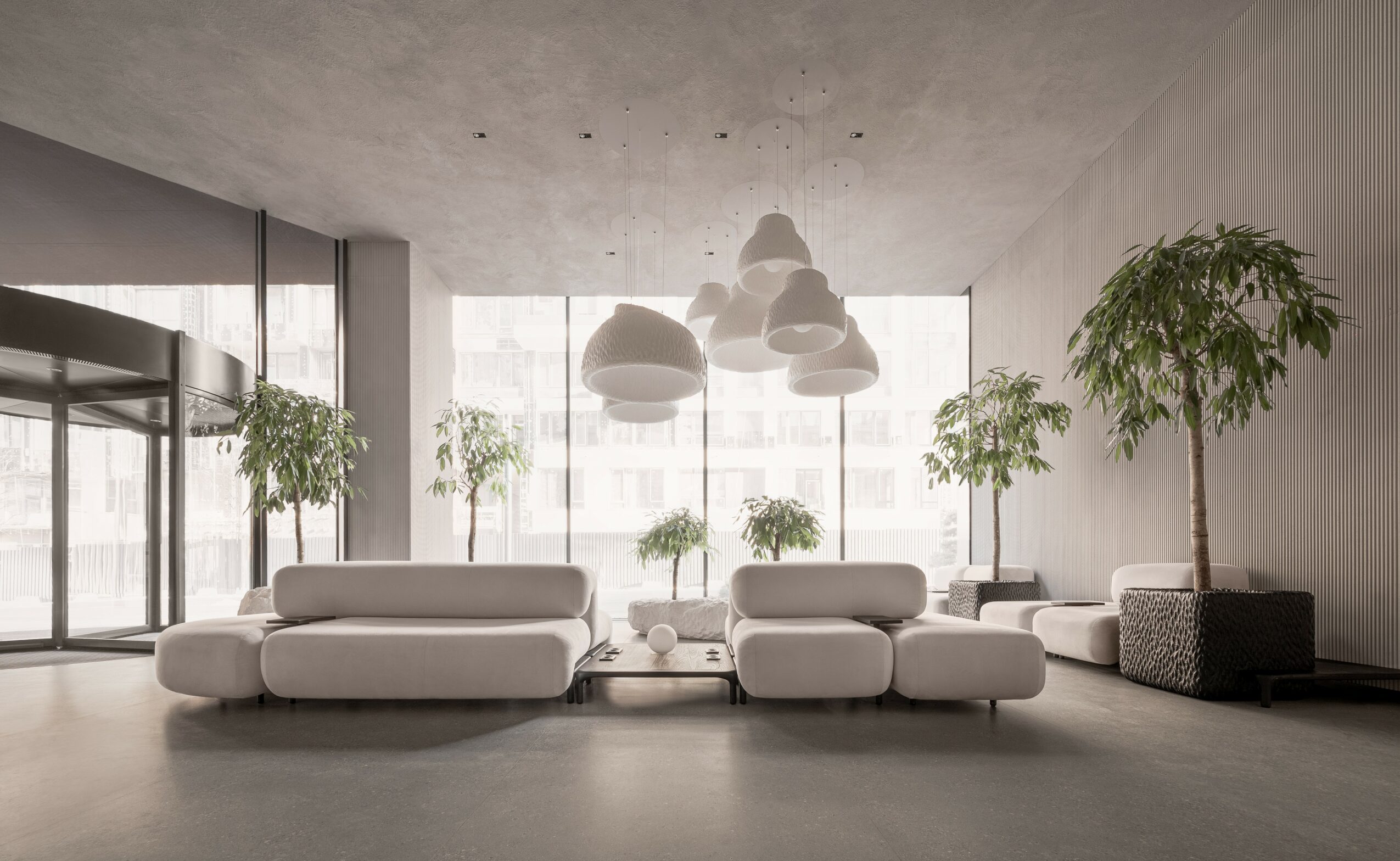 Modern lobby with large windows, white sofas, and tall potted plants, illuminated by hanging pendant lights.