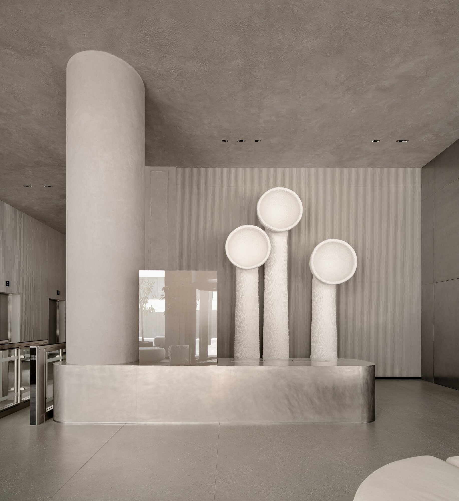 Modern interior with large cylindrical column and abstract sculpture resembling three tall, rounded shapes on a rectangular base.