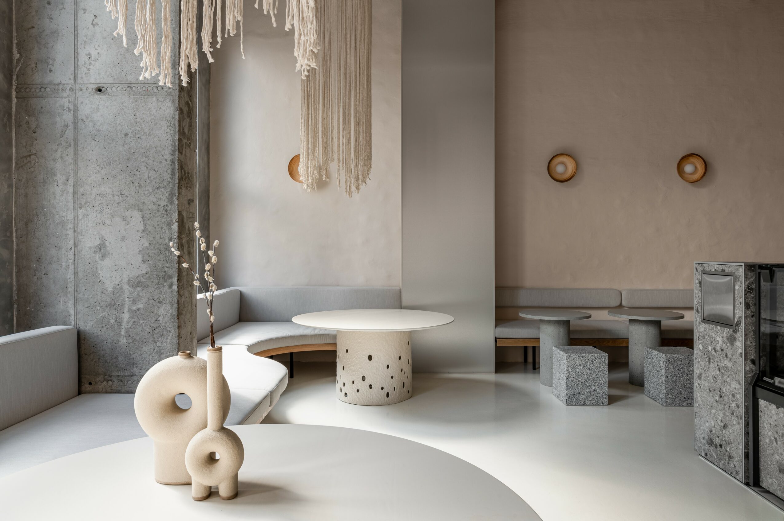 Interior space with minimalist furniture, hanging decor, and neutral tones, featuring a round table and seating area.