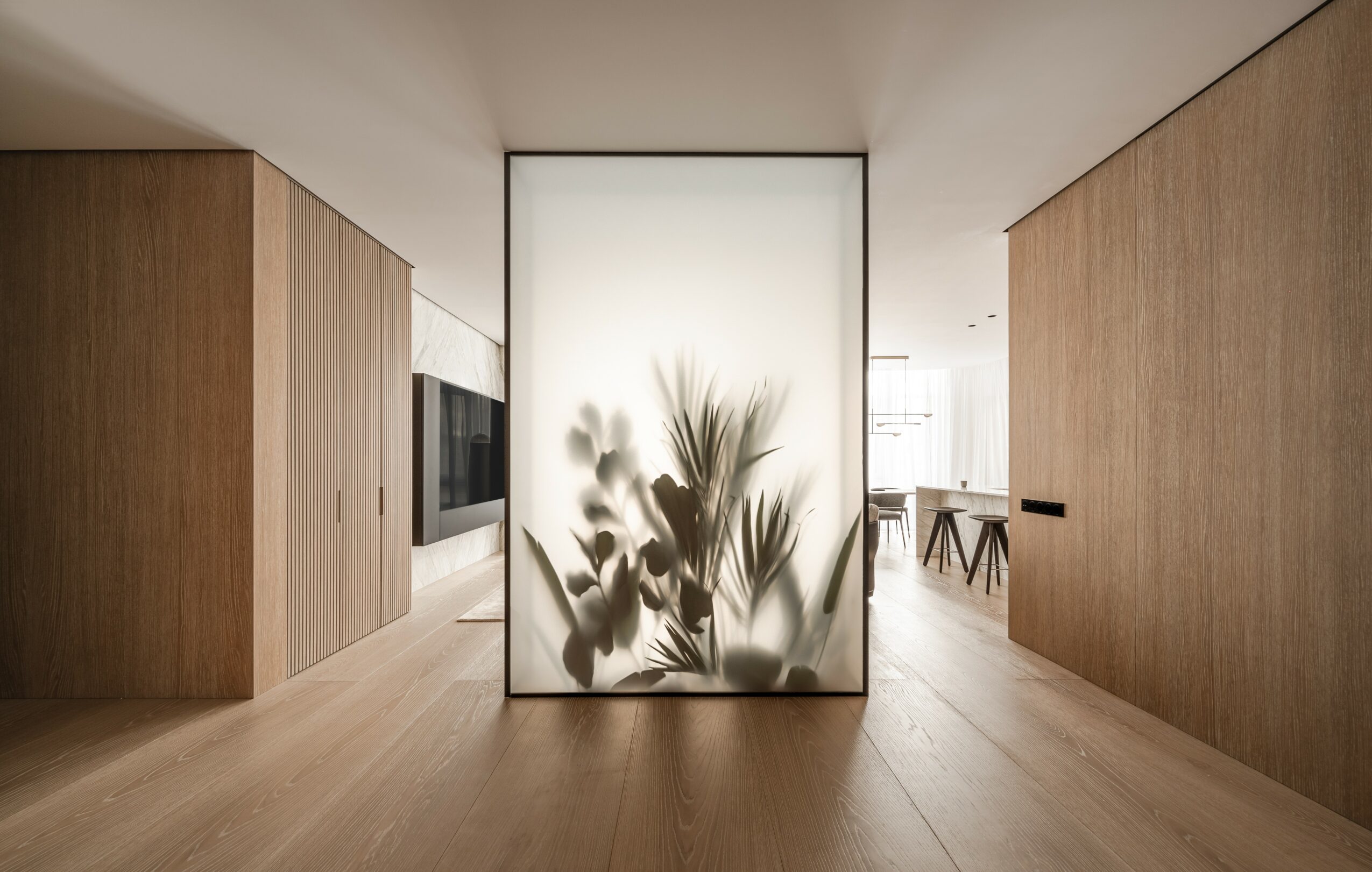 Interior space with wooden walls and floor, frosted glass panel with plant silhouette, and a dining area in the background.