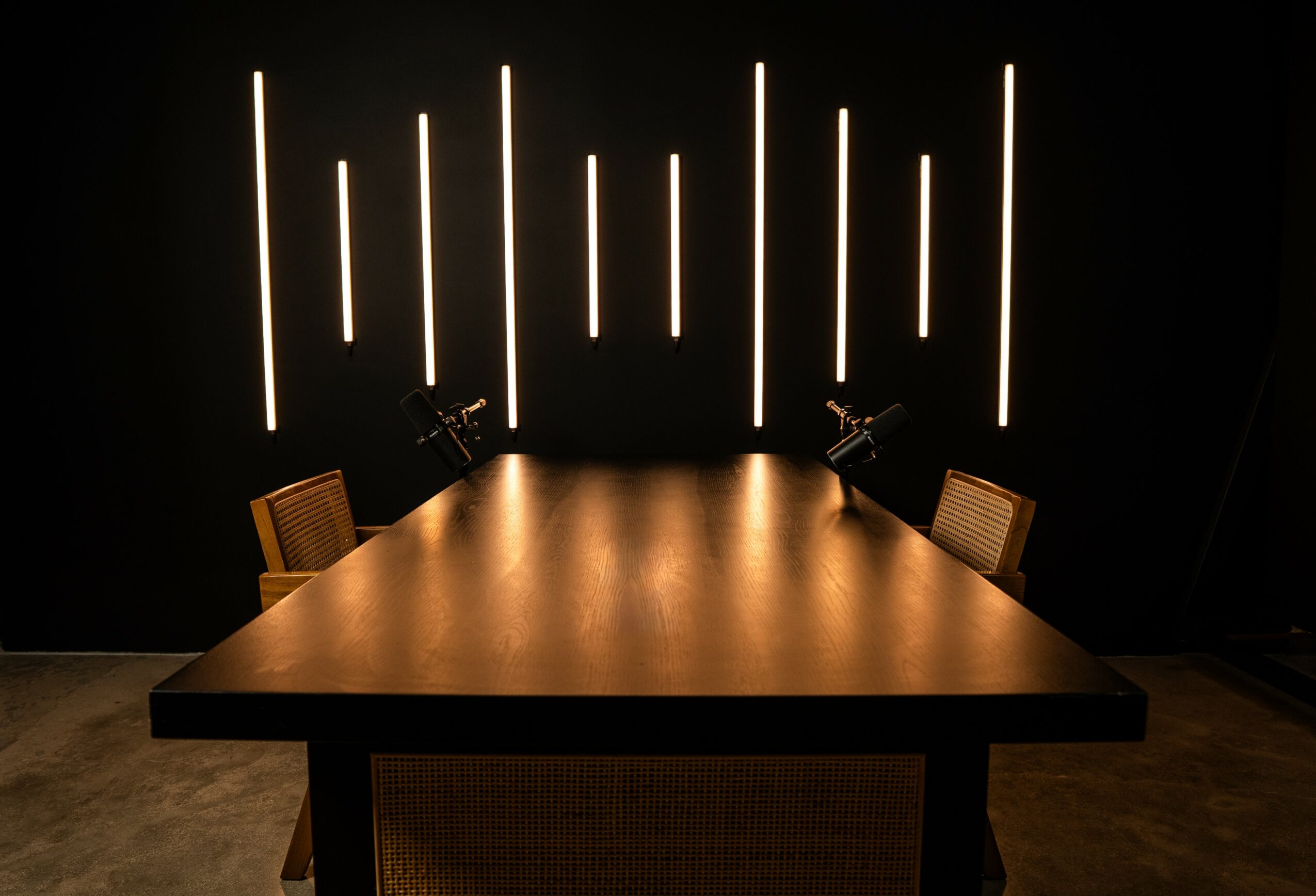 A dark room with a wooden table and two chairs, illuminated by vertical light strips on the black wall behind.