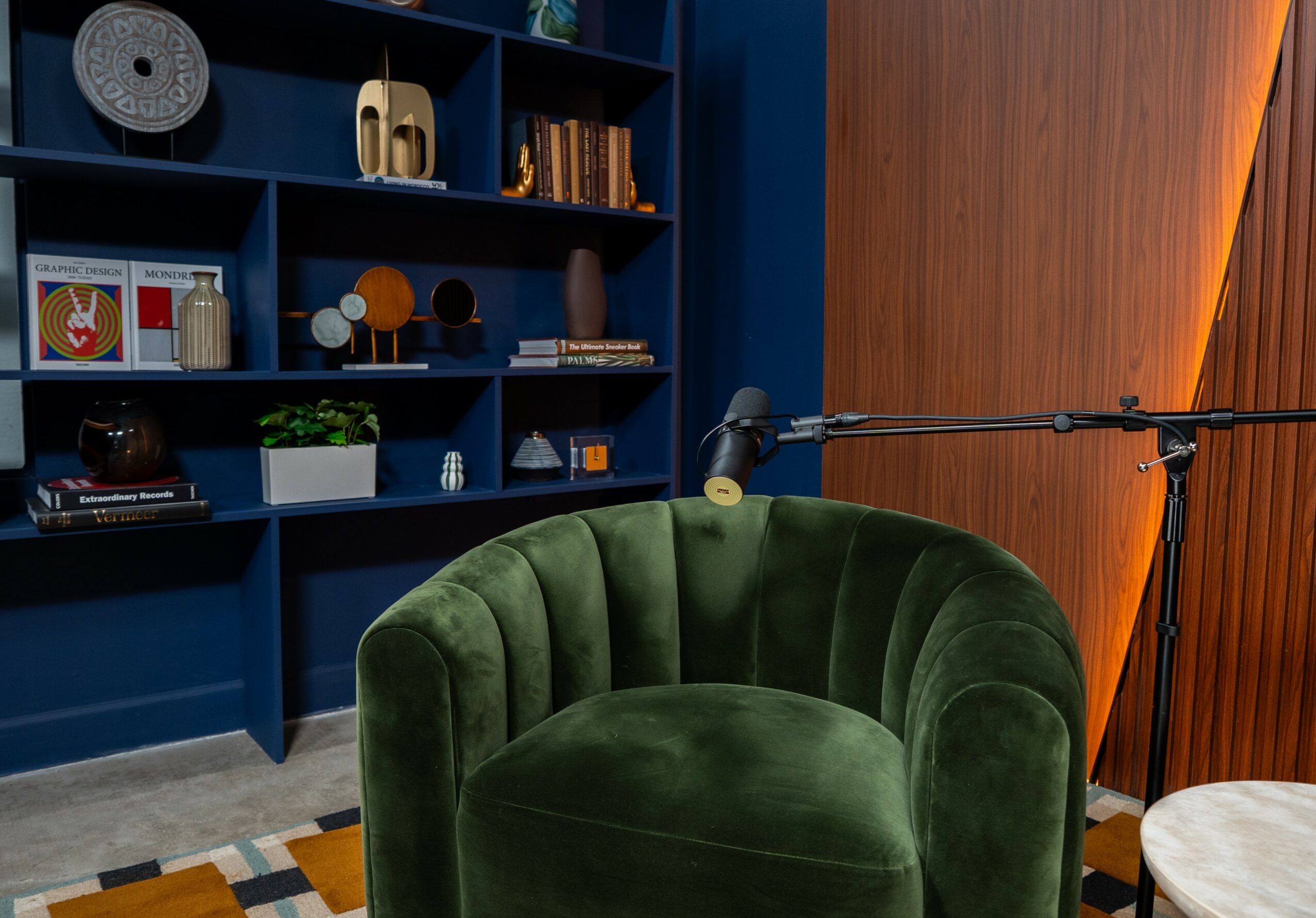 Green velvet armchair in front of a blue bookshelf with decorative items and books, against a wooden wall.