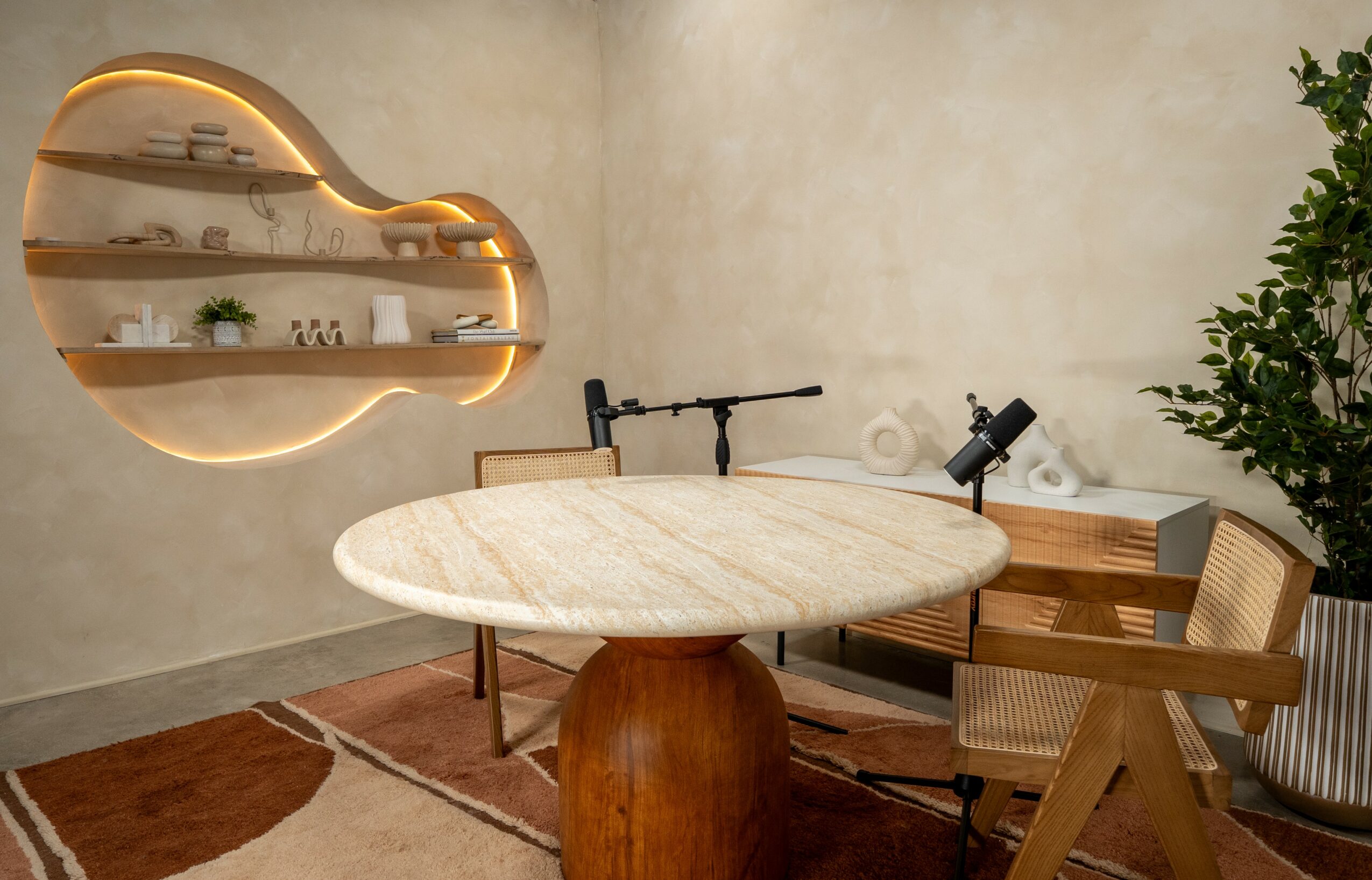 Round marble table with two chairs, wall shelf with plants, and a large plant in a room.