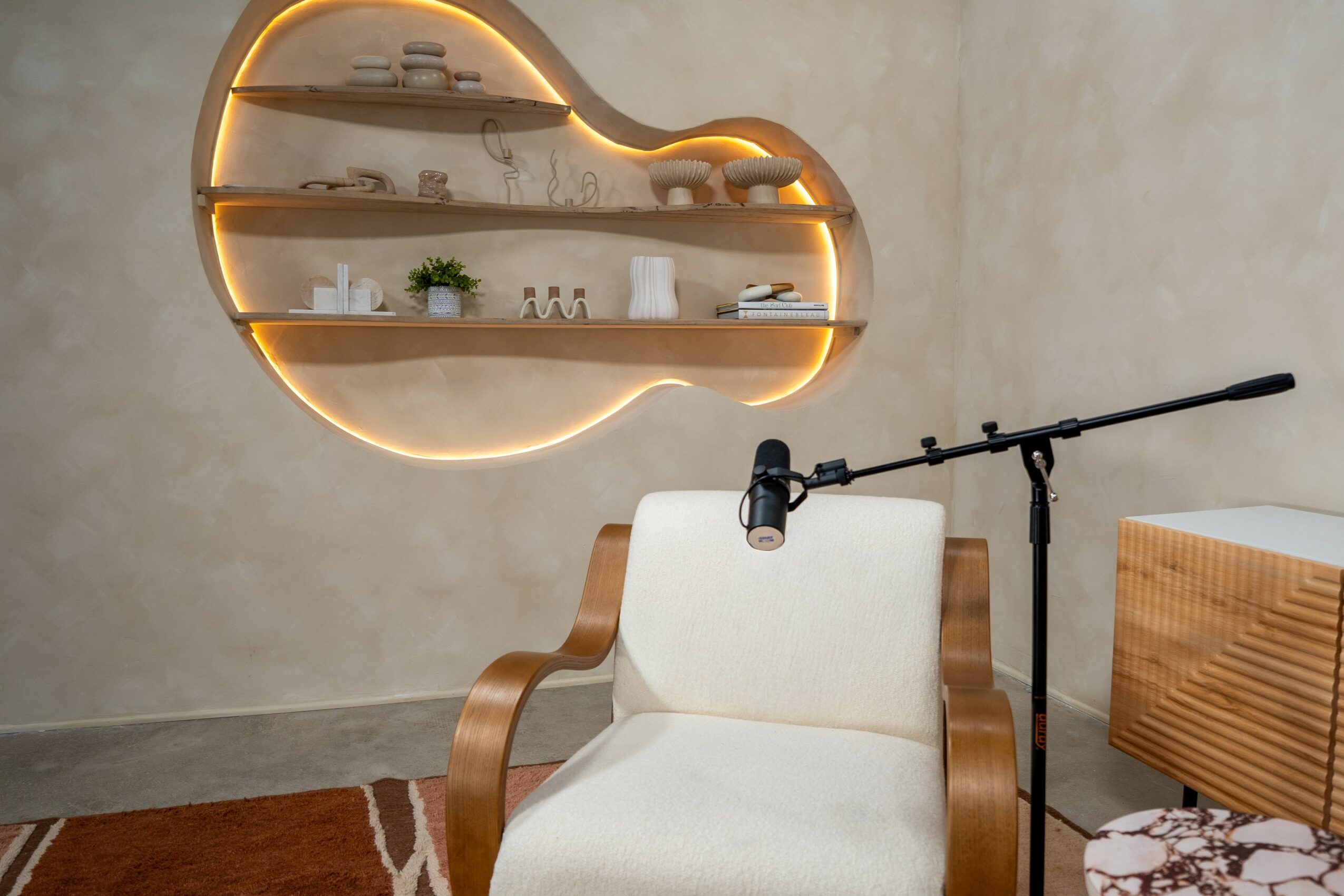 Interior room with a cloud-shaped wall shelf, a white armchair, a microphone stand, and a wooden side table.