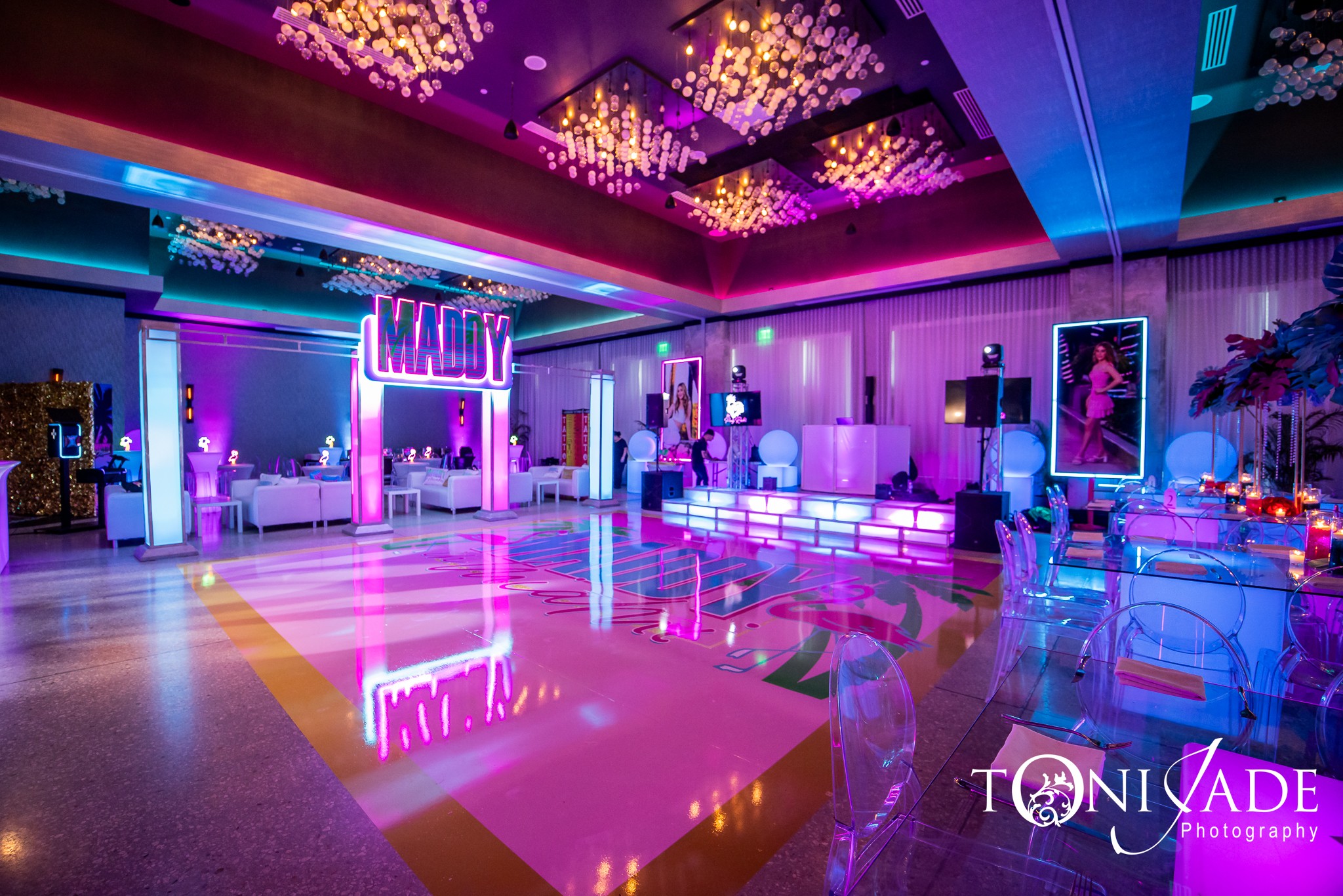 Empty event space with colorful lighting, a dance floor, and seating areas, decorated with neon signs and artwork.