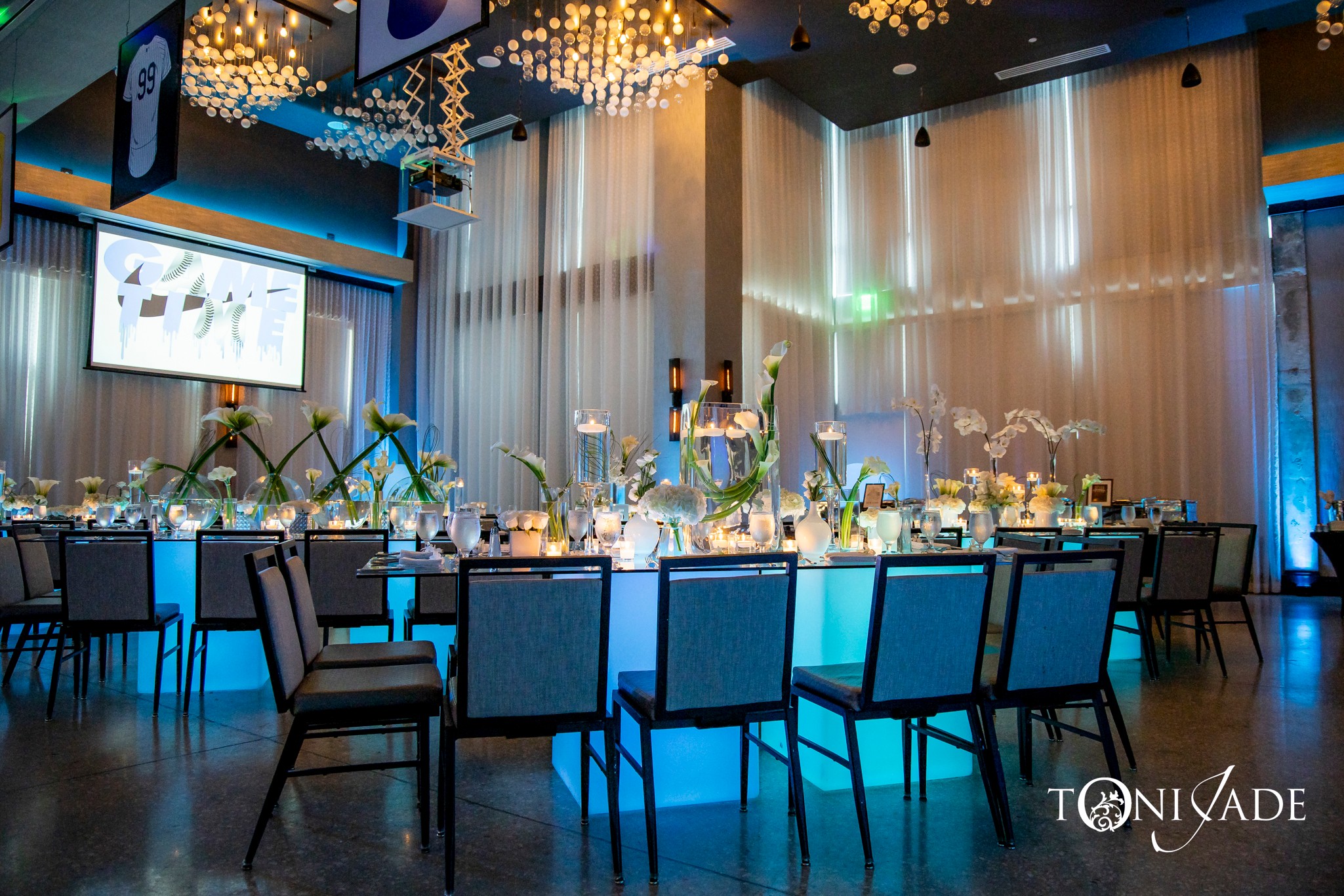 Elegant banquet hall with decorated tables, floral centerpieces, and hanging lights, illuminated with blue and warm lighting.