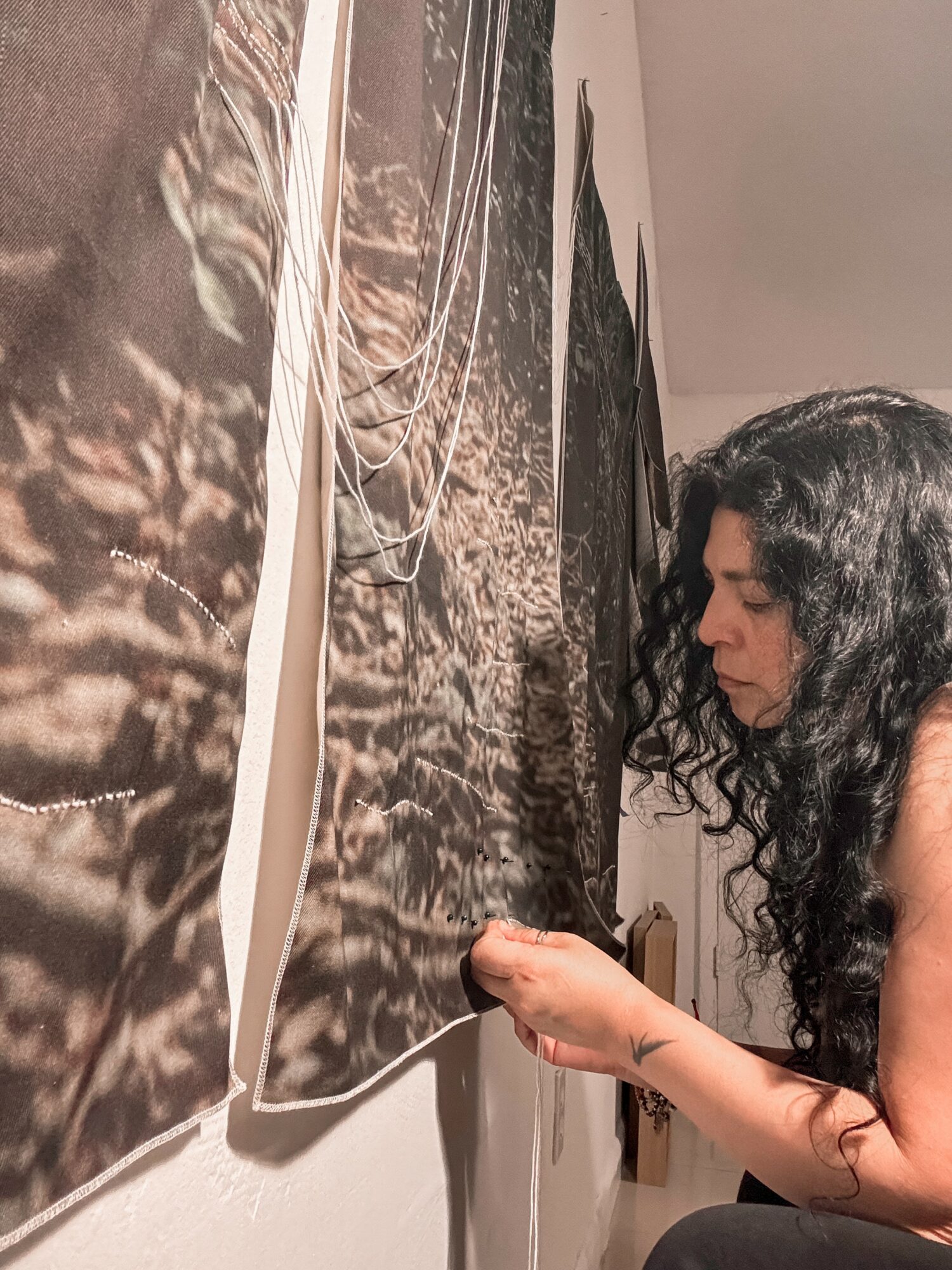 Woman with curly hair looking at artwork on wall, holding a small object in her hand.