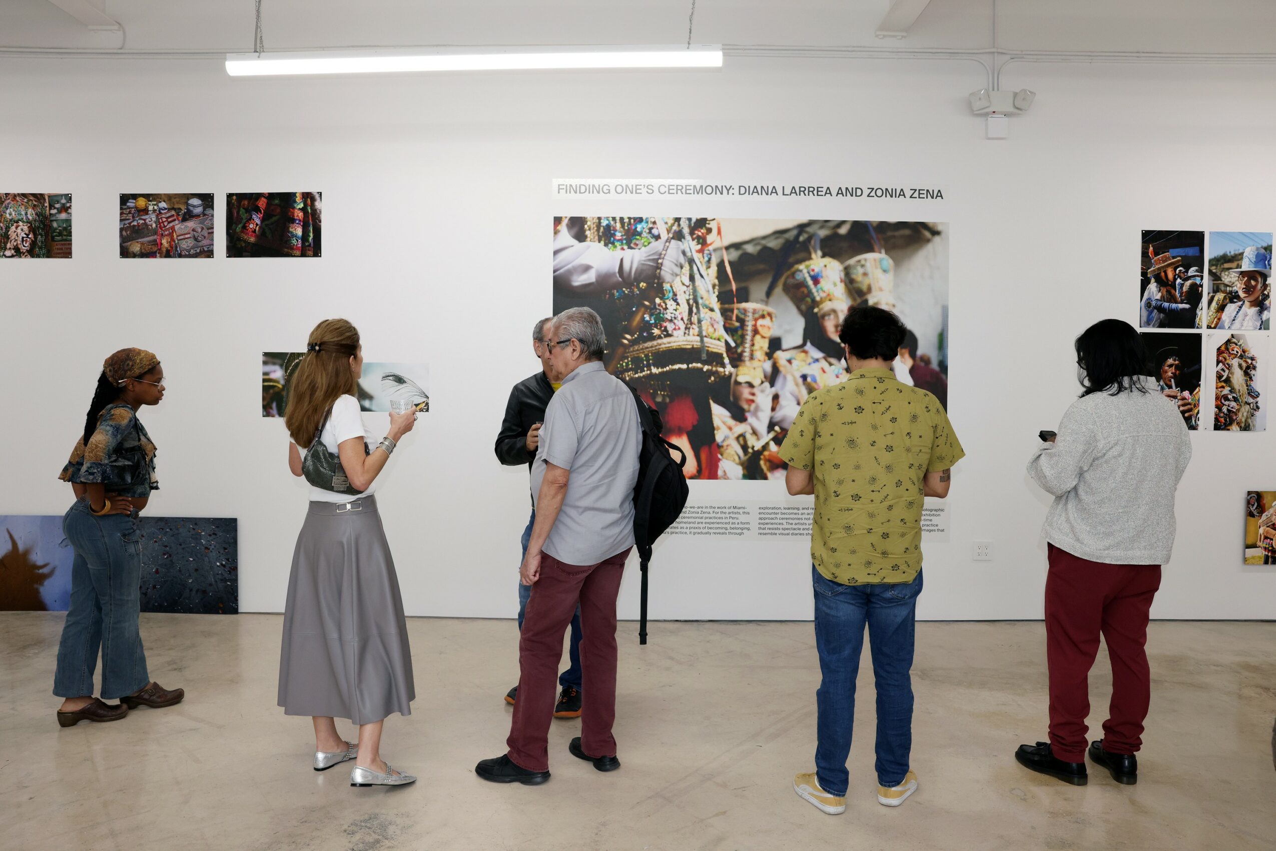 People viewing artwork in a gallery, some taking photos, with framed pictures on white walls.