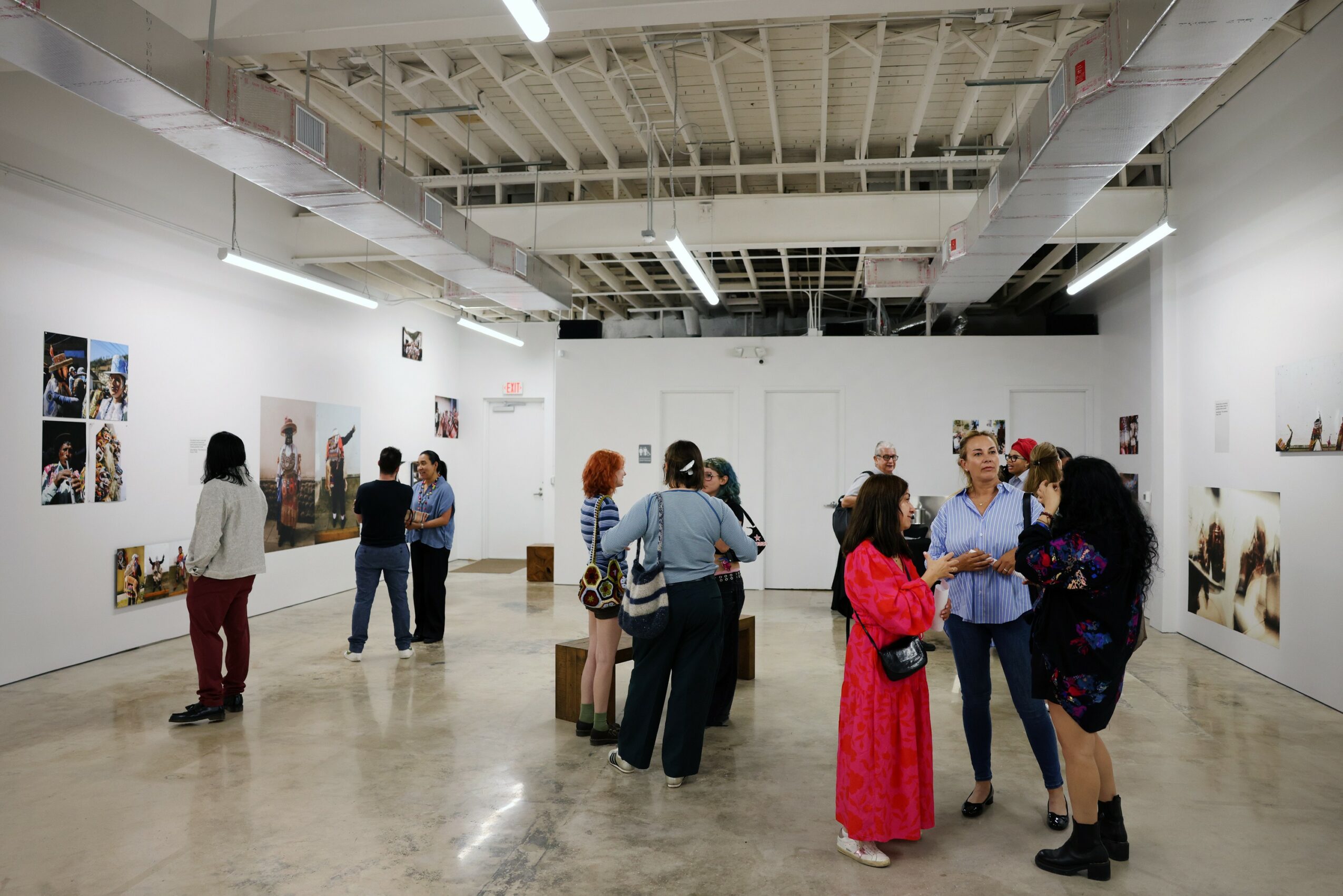 People viewing artwork in a spacious gallery with white walls and ceiling, some engaging in conversation, others observing art pieces.