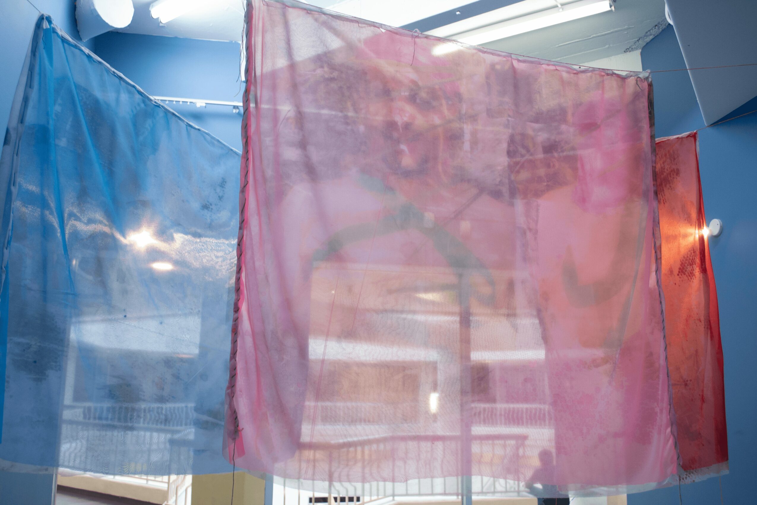 Colorful translucent curtains hanging indoors, with sunlight shining through, creating reflections and shadows.