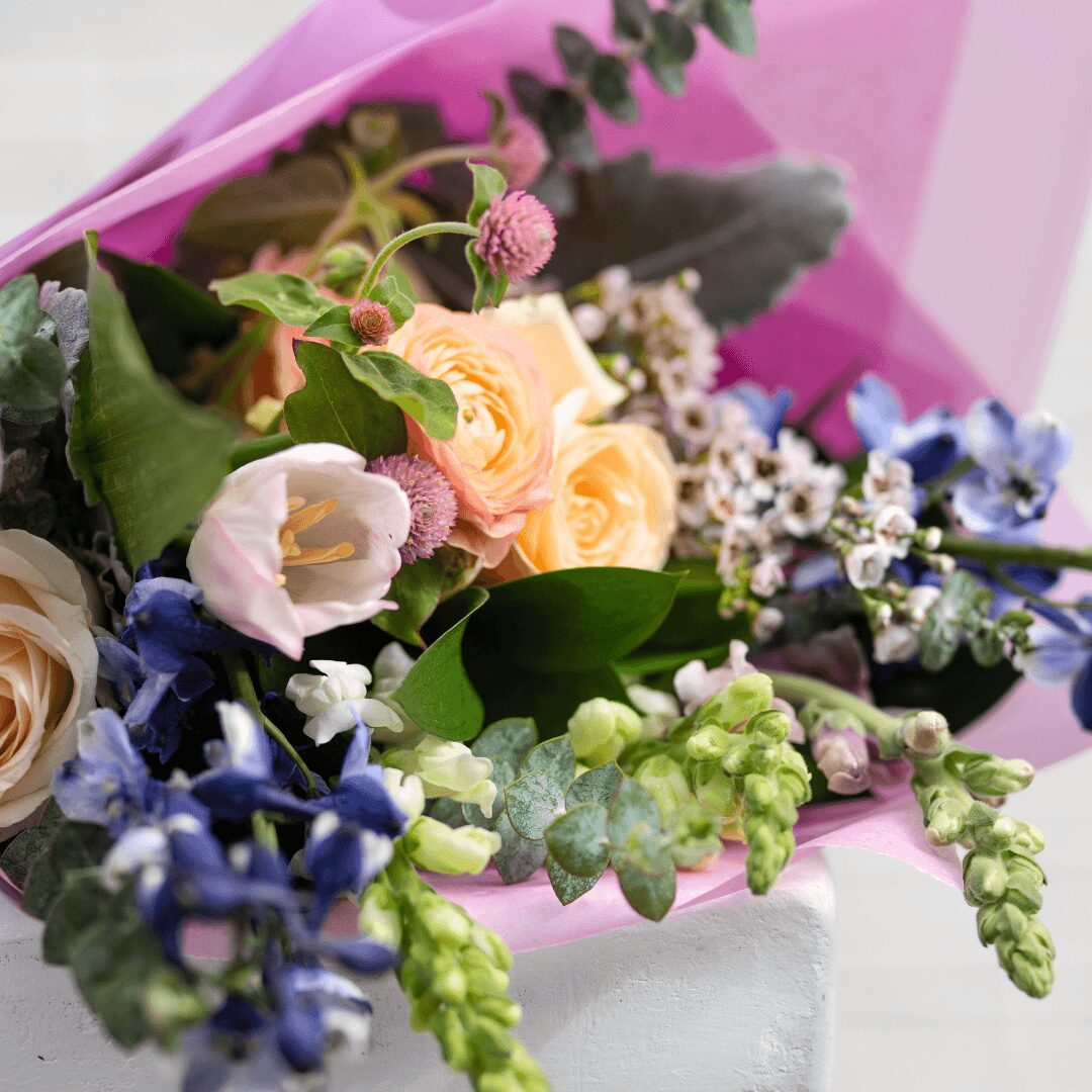 Colorful bouquet of flowers with pink, yellow, white, purple, and green blooms wrapped in pink paper.