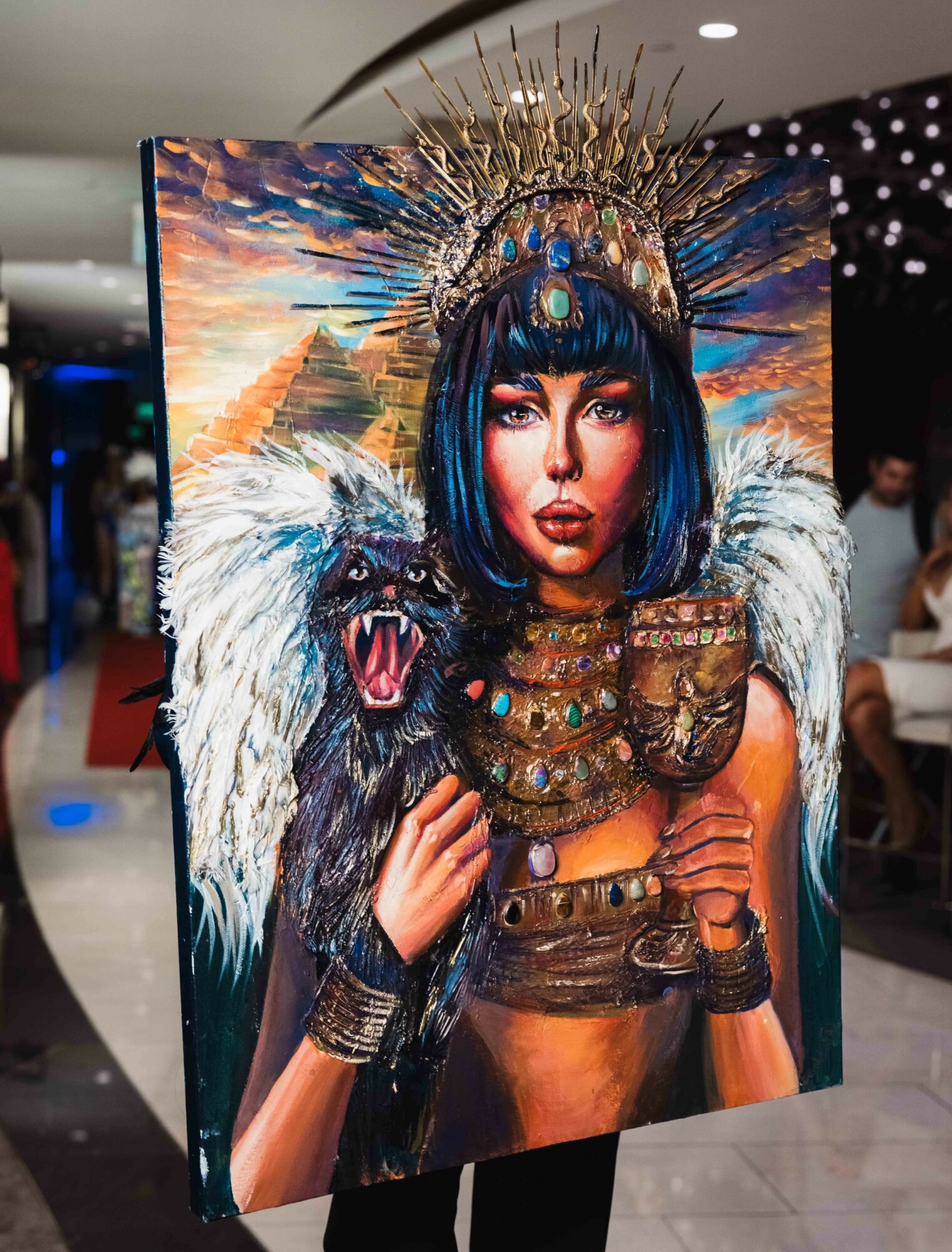 Woman with blue hair, elaborate crown, and jewelry holding a lion's head, in a costume with fur and metallic accessories.