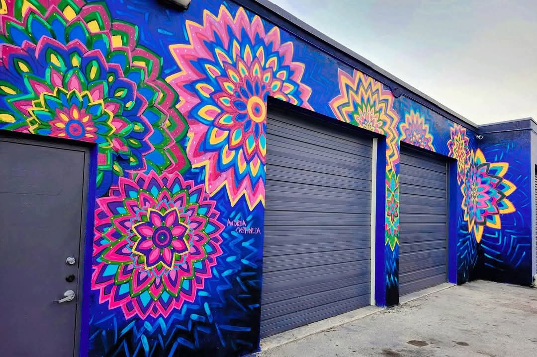 Colorful mural with large, intricate mandala patterns on a building wall, featuring three garage doors, vibrant blue background.