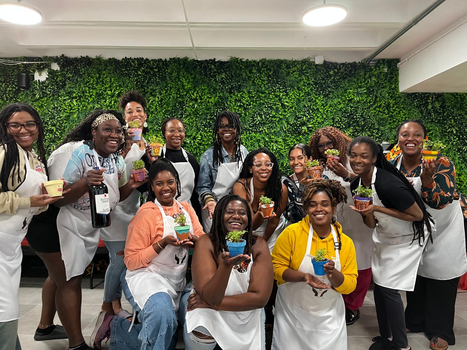 Group of people smiling and holding food and drinks in front of a green wall, indoors.