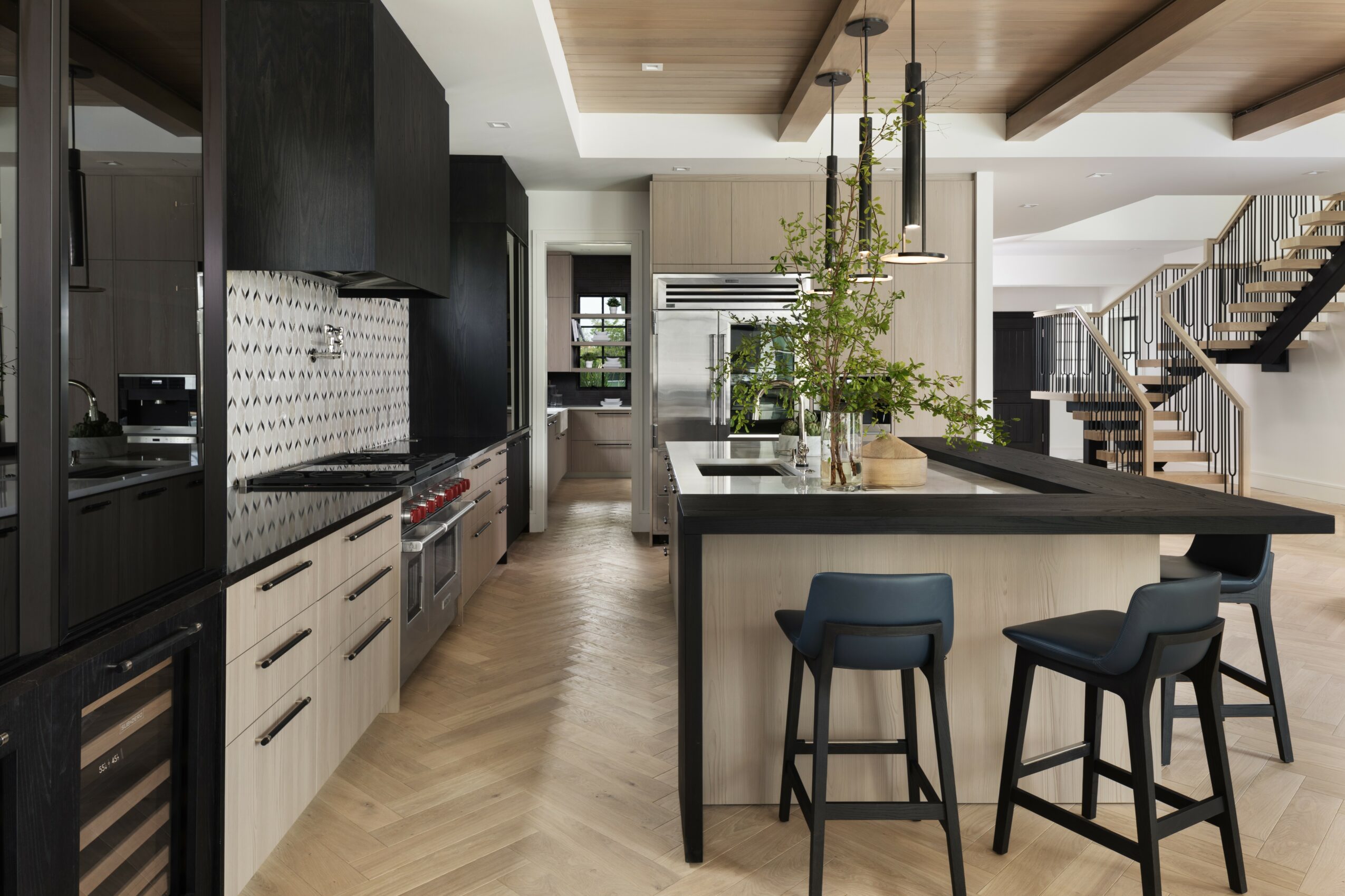 Modern kitchen with black and white cabinets, a large island with two stools, and a staircase in the background.