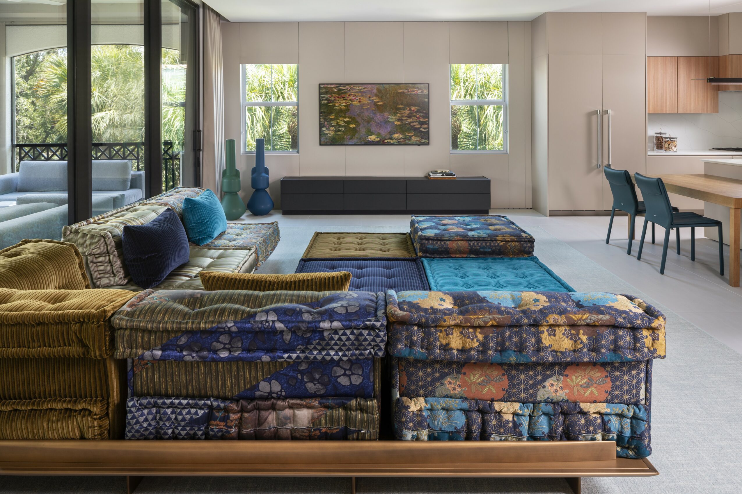 Living room with large window, sofa, colorful ottomans, and a wall-mounted TV, bright and modern interior.