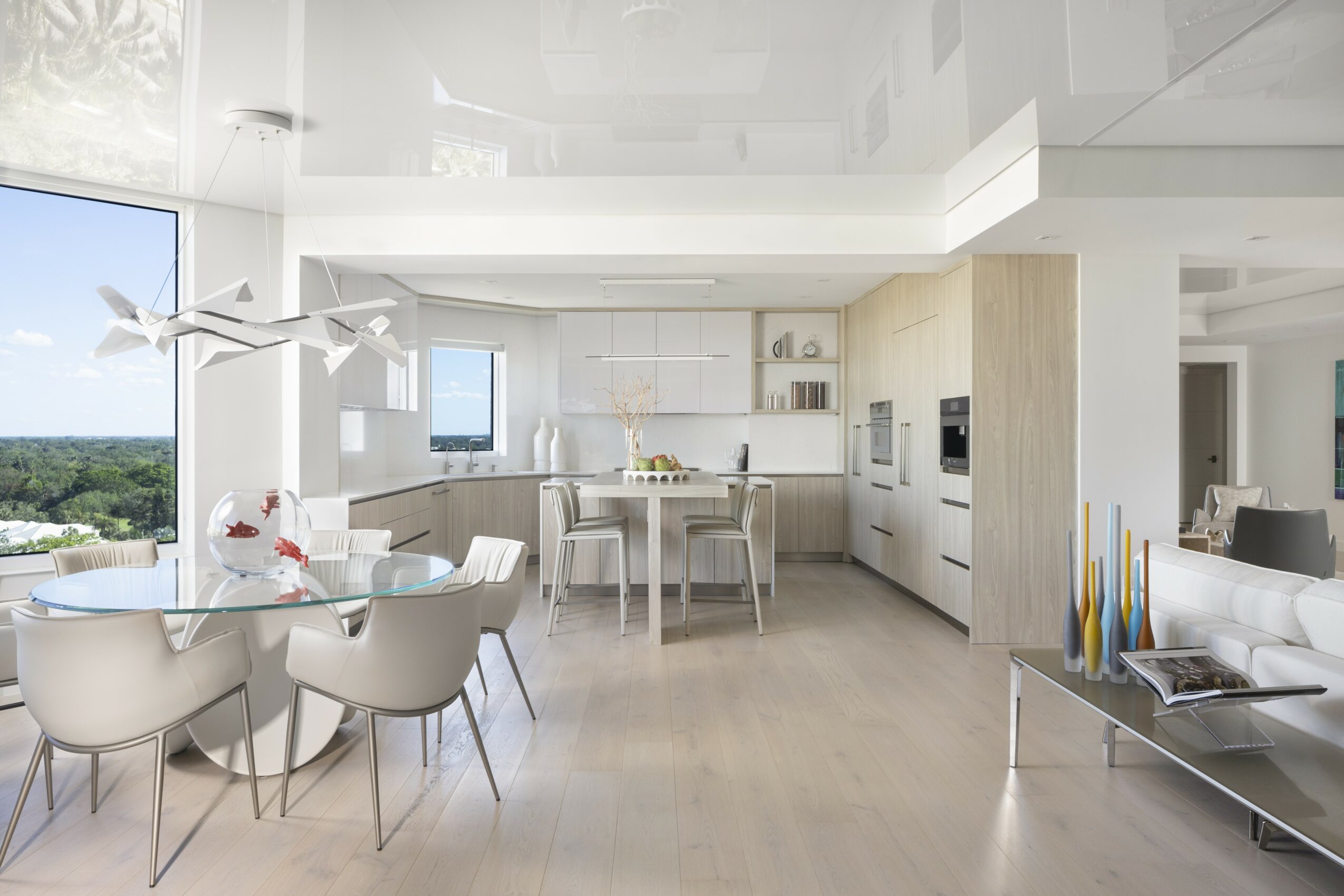Modern kitchen and dining area with white furniture, large windows, and light-colored flooring.