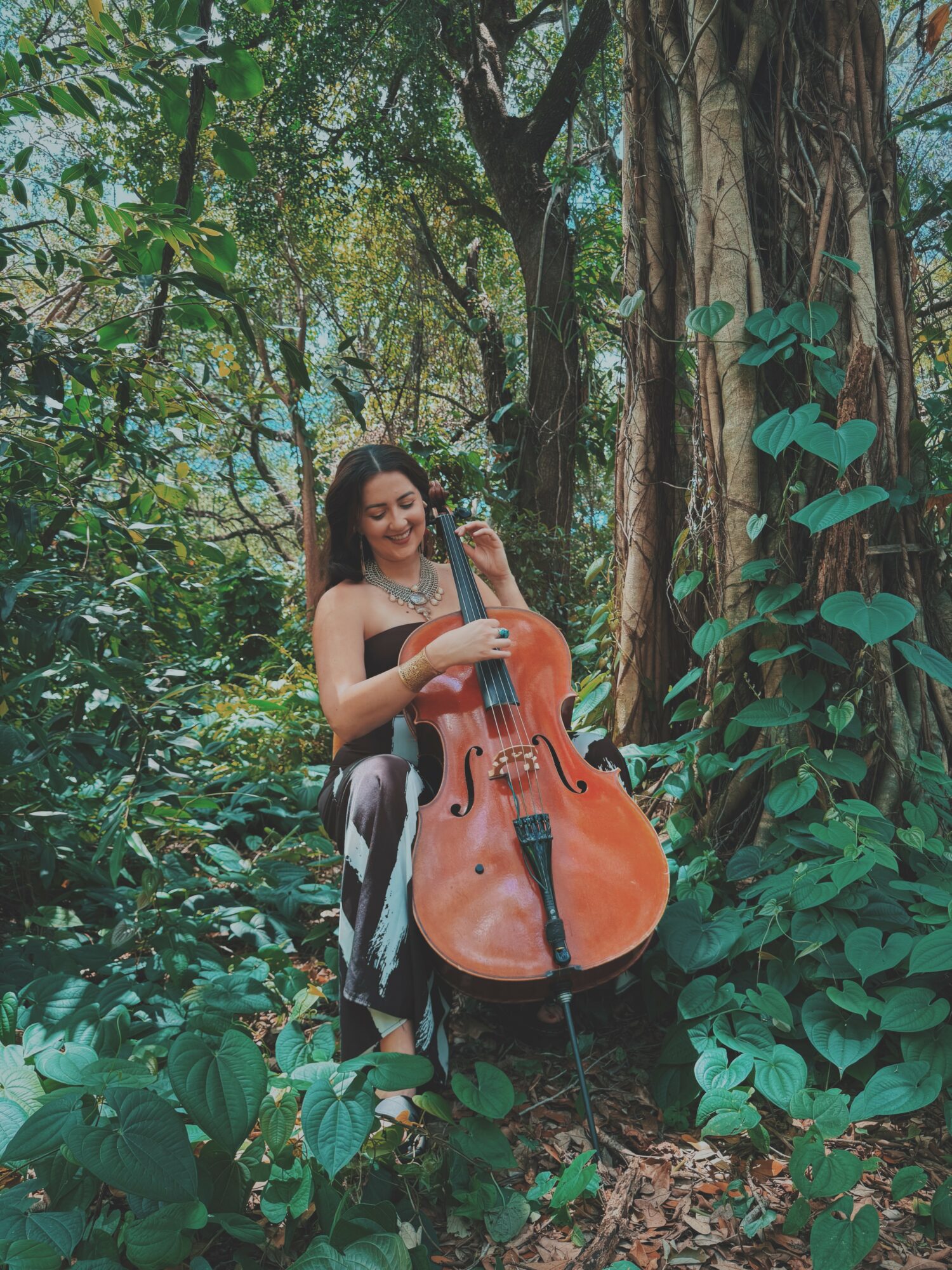 Woman playing cello in a lush forest surrounded by green foliage and trees.