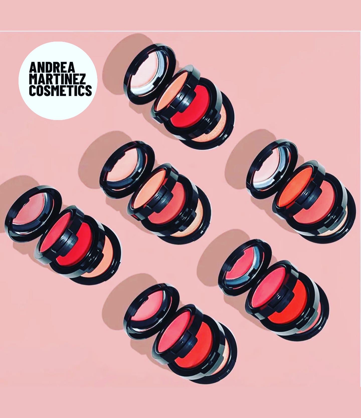 Multiple black and red cosmetic containers arranged on a pink background with shadows, and a white circle with black text reading 'Andrea Martinez Cosmetics'.