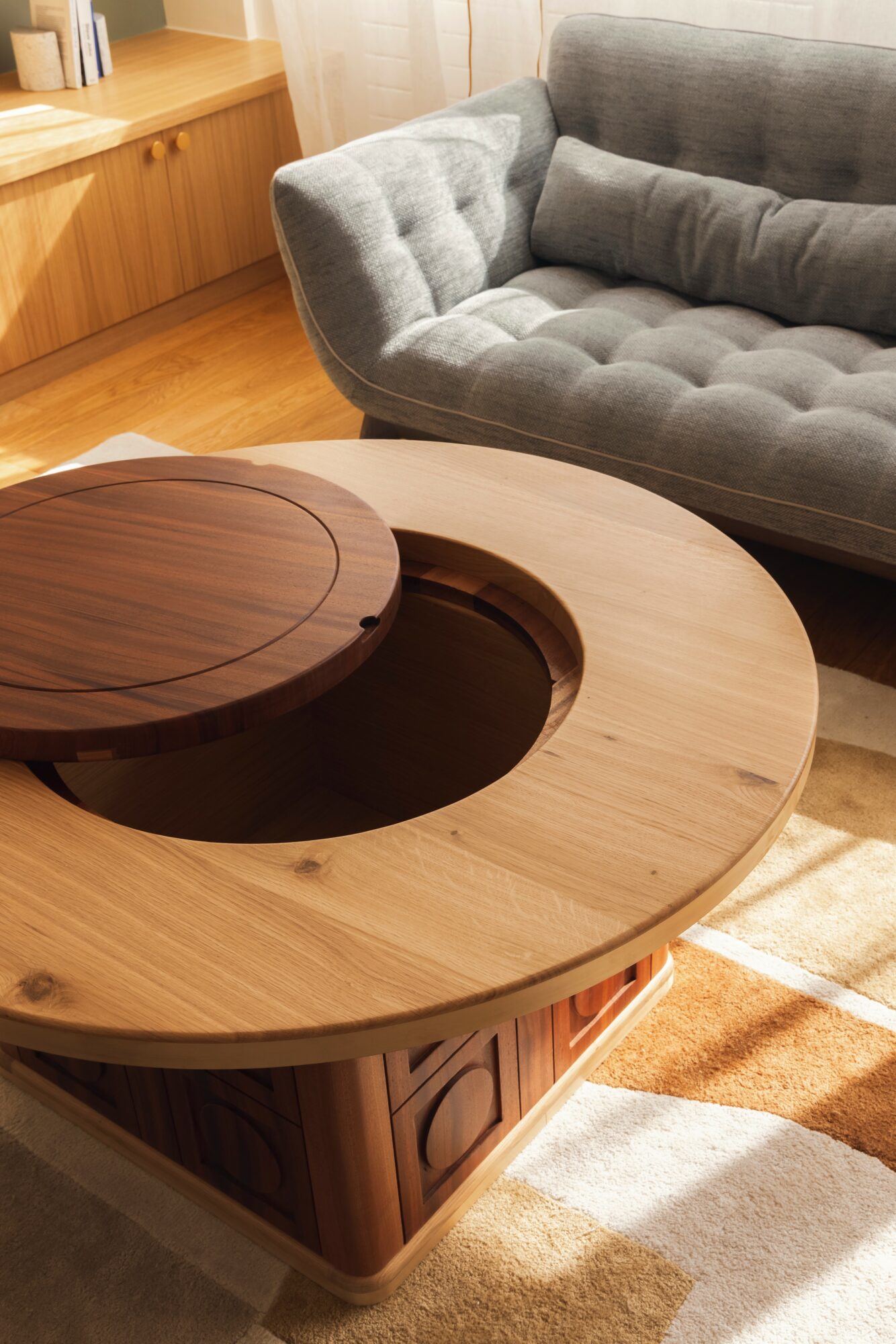 Round wooden table with a hollow center, placed in a living room with a gray sofa and wooden furniture.