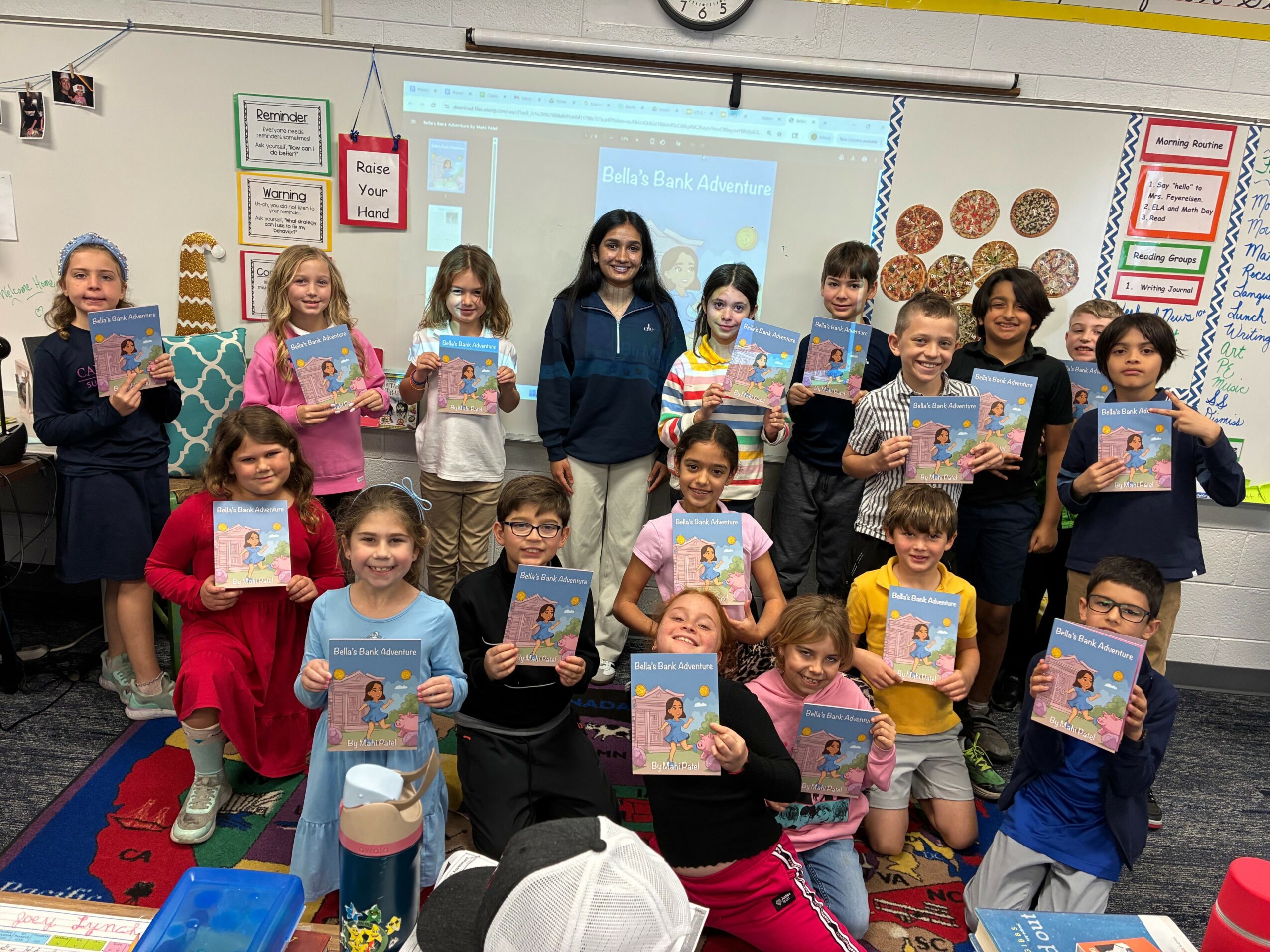 Group of children and teacher in classroom holding books, standing and sitting, with whiteboard and colorful decorations behind them.