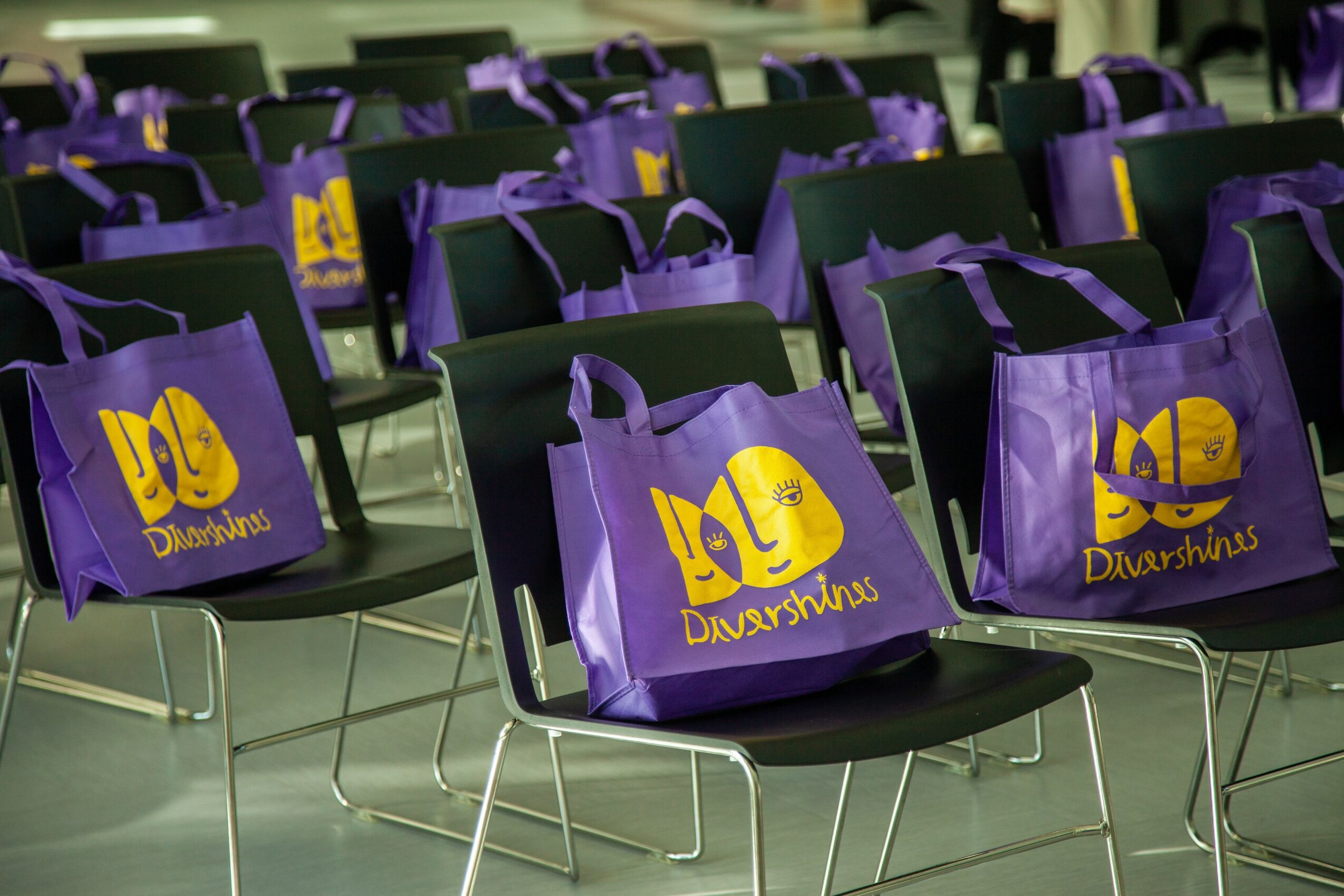 Multiple purple bags with yellow logo on black chairs in a room, arranged in rows.