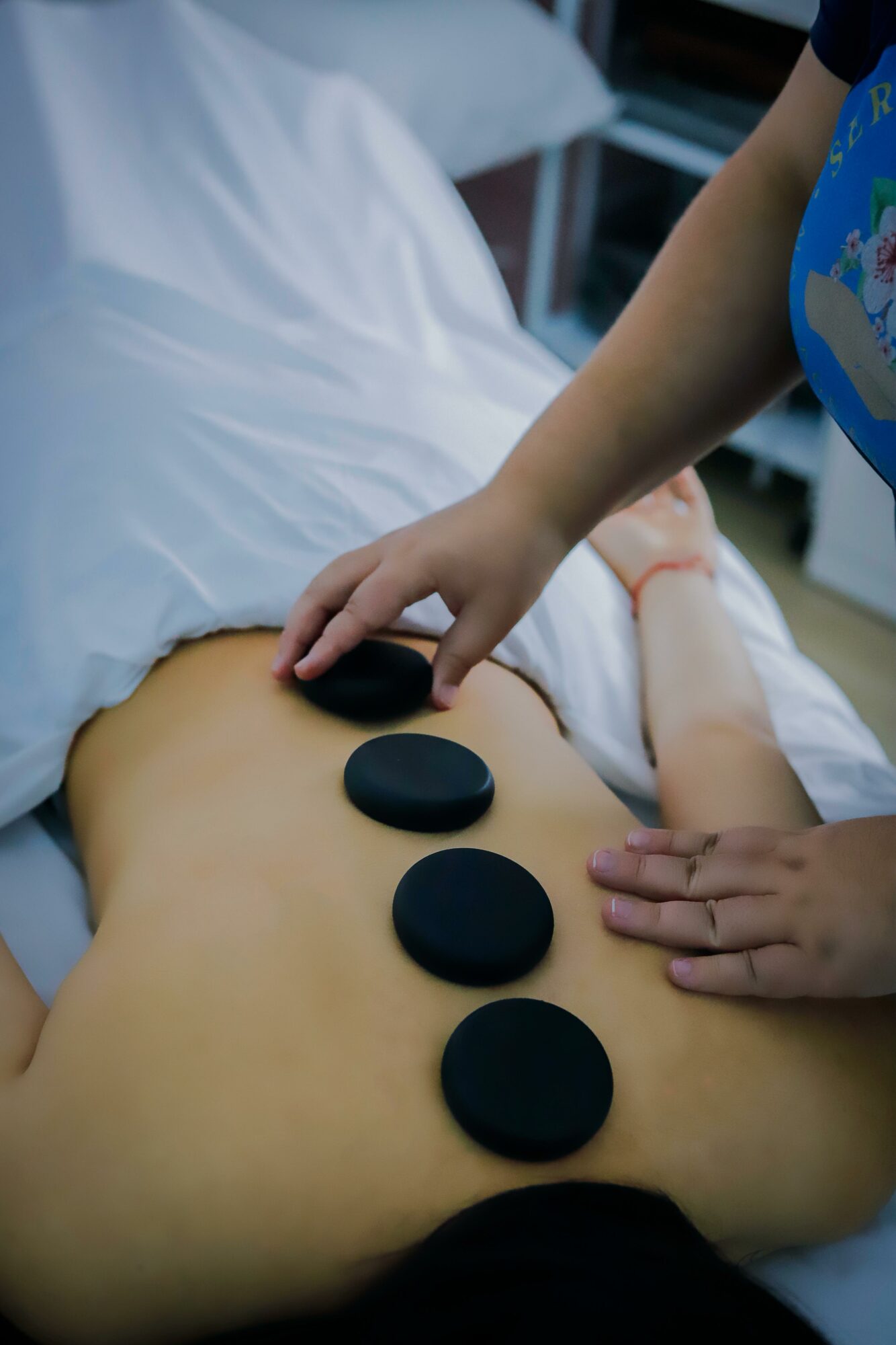 Child places smooth black stones on a person's bare abdomen during a therapy session.